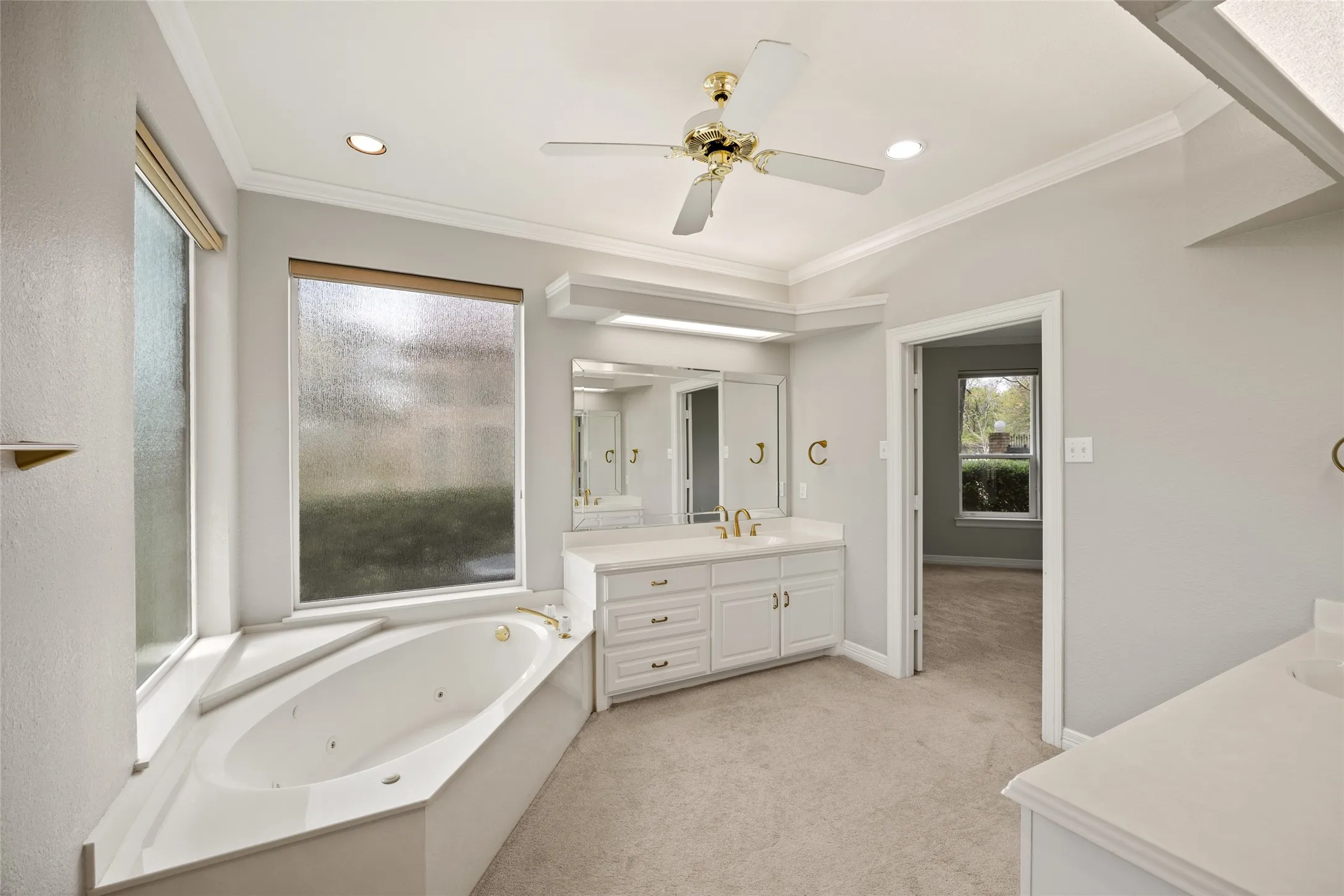 Bathroom with light carpet, two vanities, a whirlpool tub, ceiling fan, and crown molding