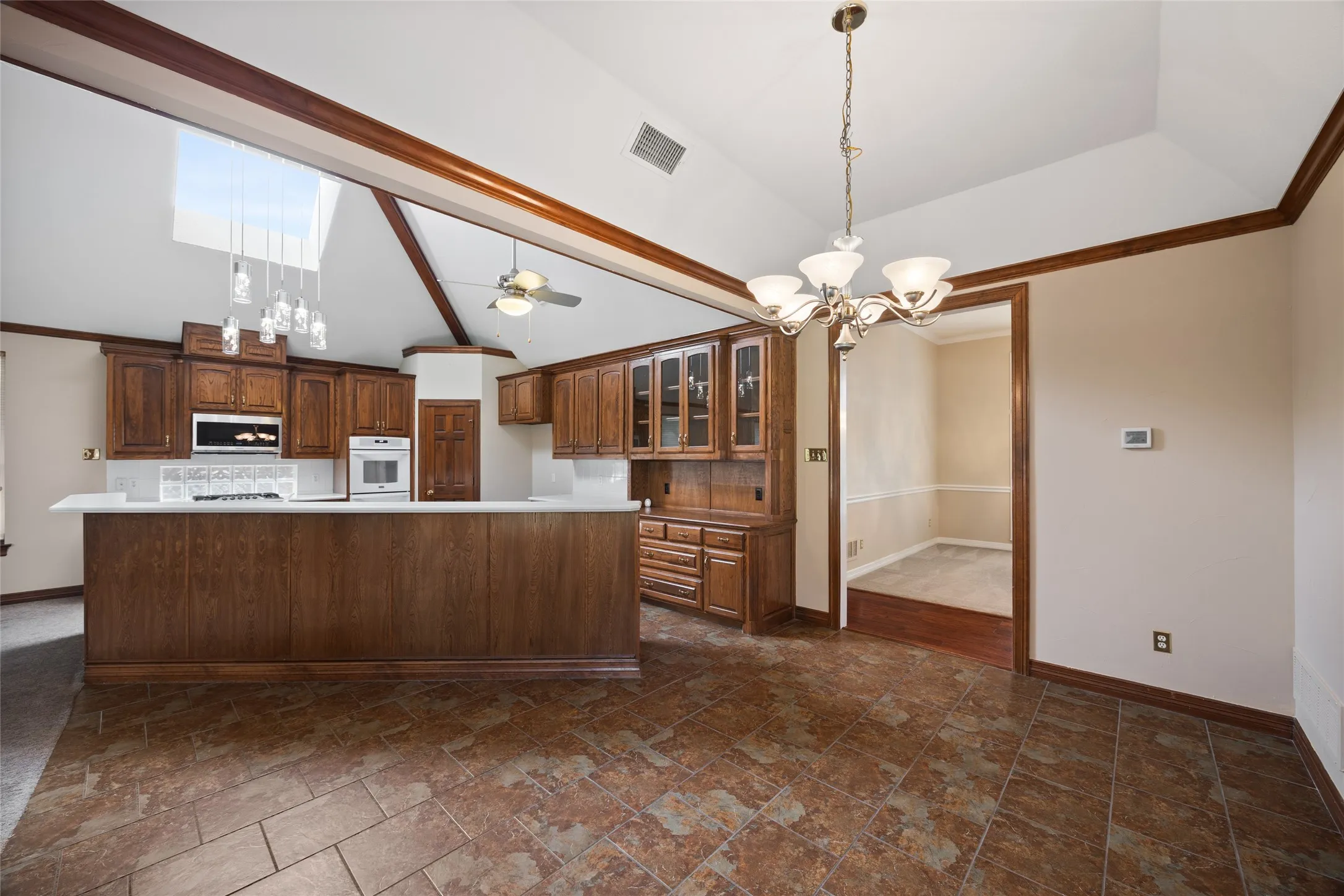 Kitchen with suspended lighting, dark stone finish floors, light countertops, vaulted ceiling, and a ceiling fan
