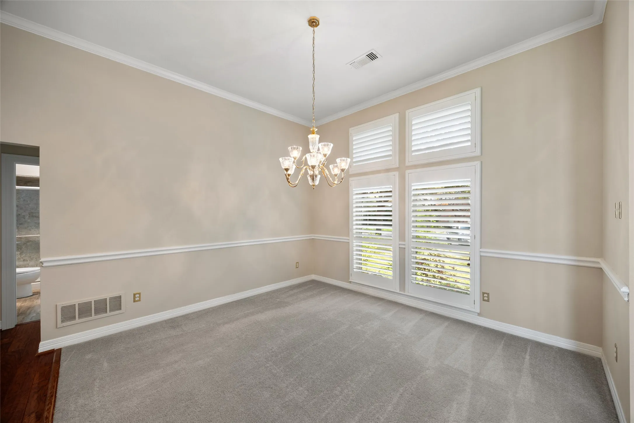 Empty room with hanging lights, crown molding, and dark carpet
