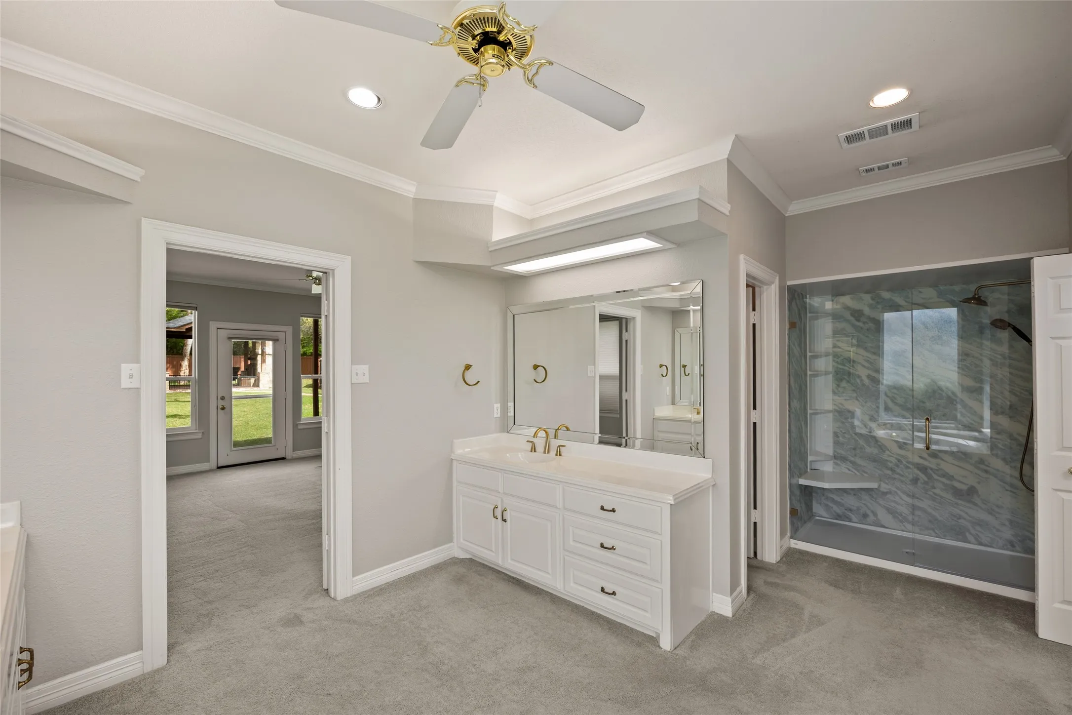 Full bath featuring ceiling fan, vanity, a marble finish shower, crown molding, and light colored carpet