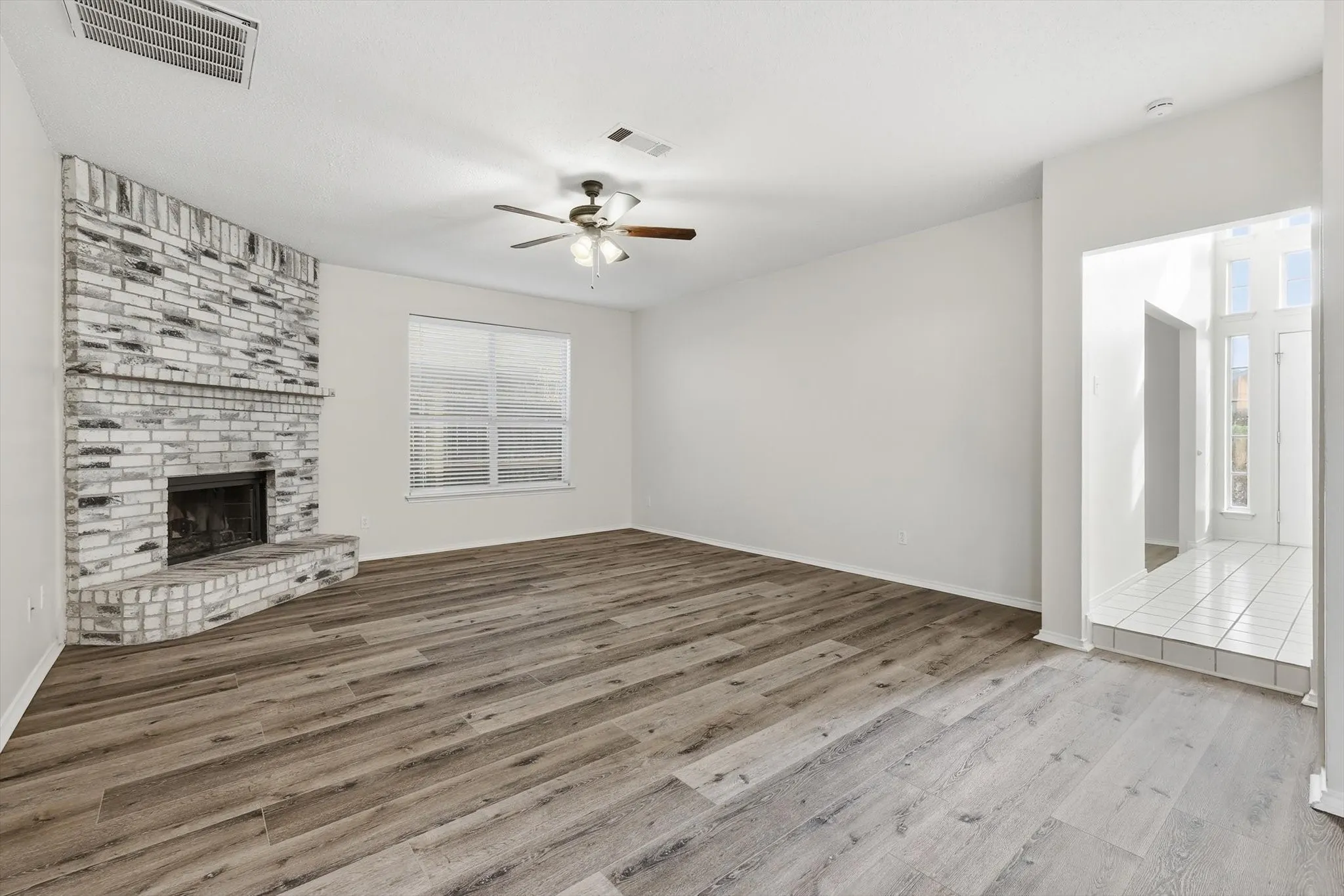 Unfurnished living room with a brick fireplace, light wood-style floors, and a ceiling fan
