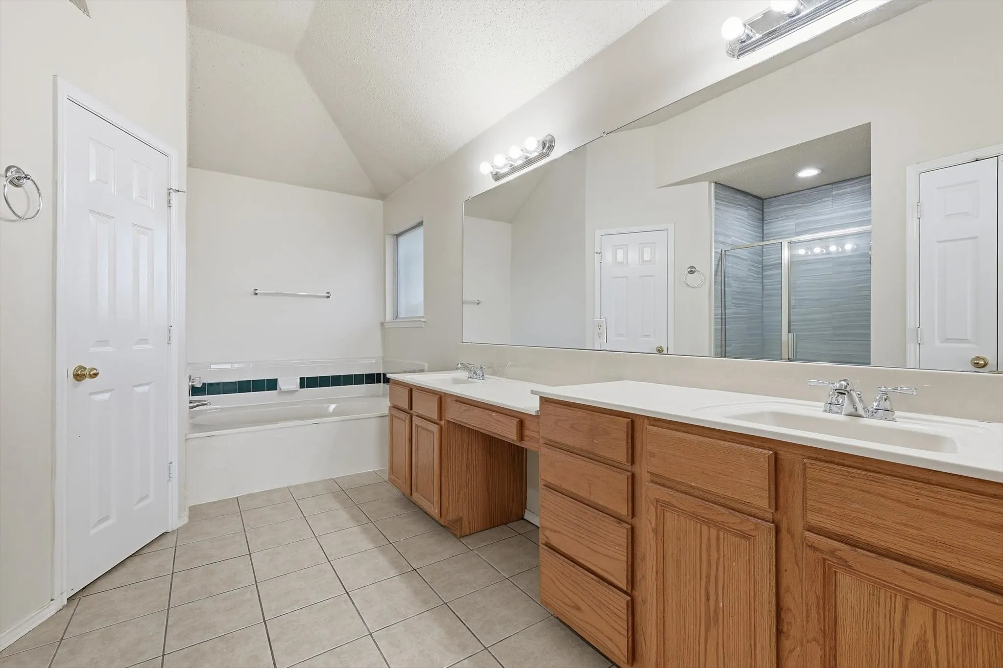 Bathroom with lofted ceiling, double vanity, light tile patterned floors, a stall shower, and a bath