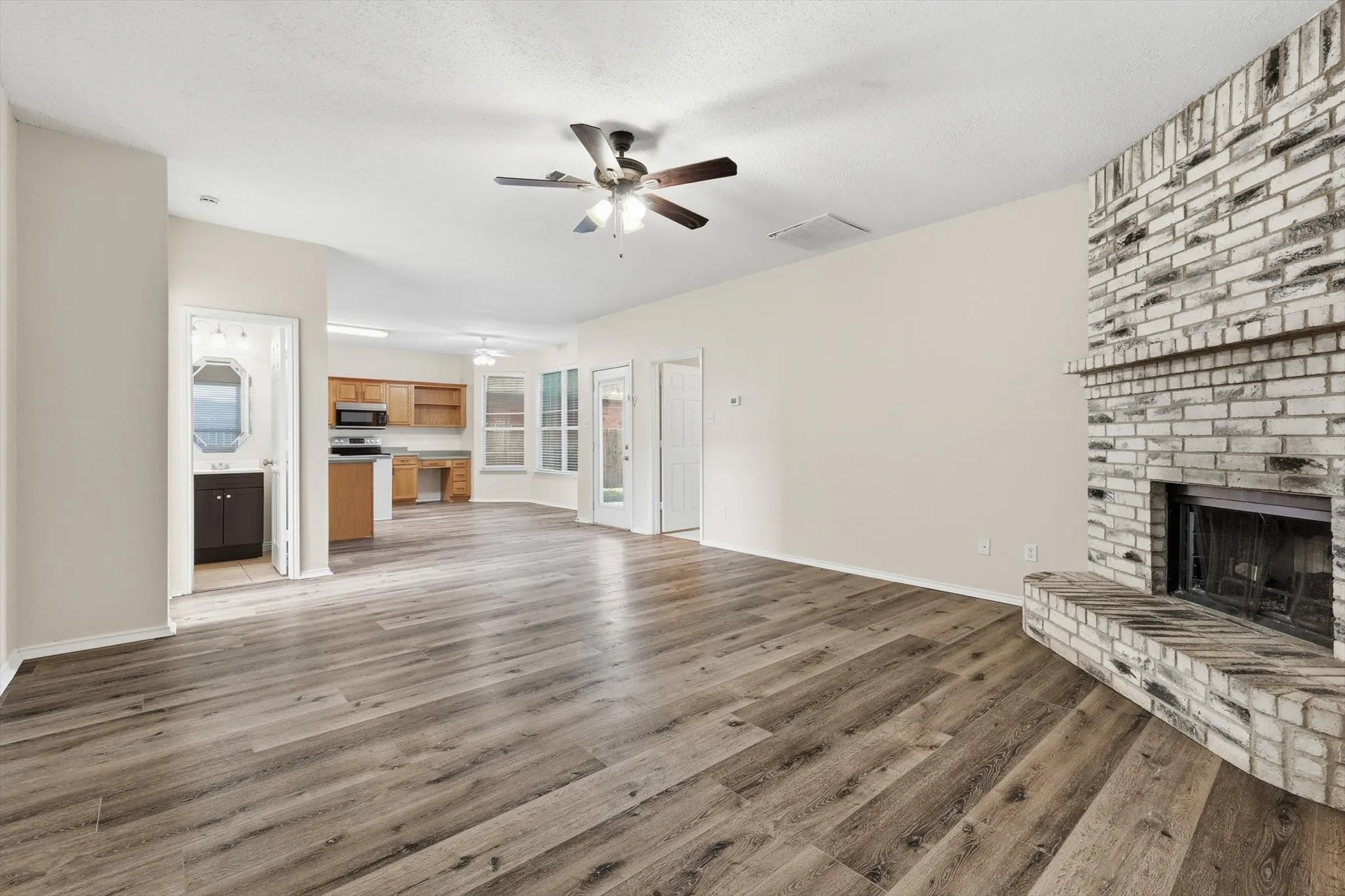 Unfurnished living room featuring a brick fireplace, light wood finished floors, and ceiling fan