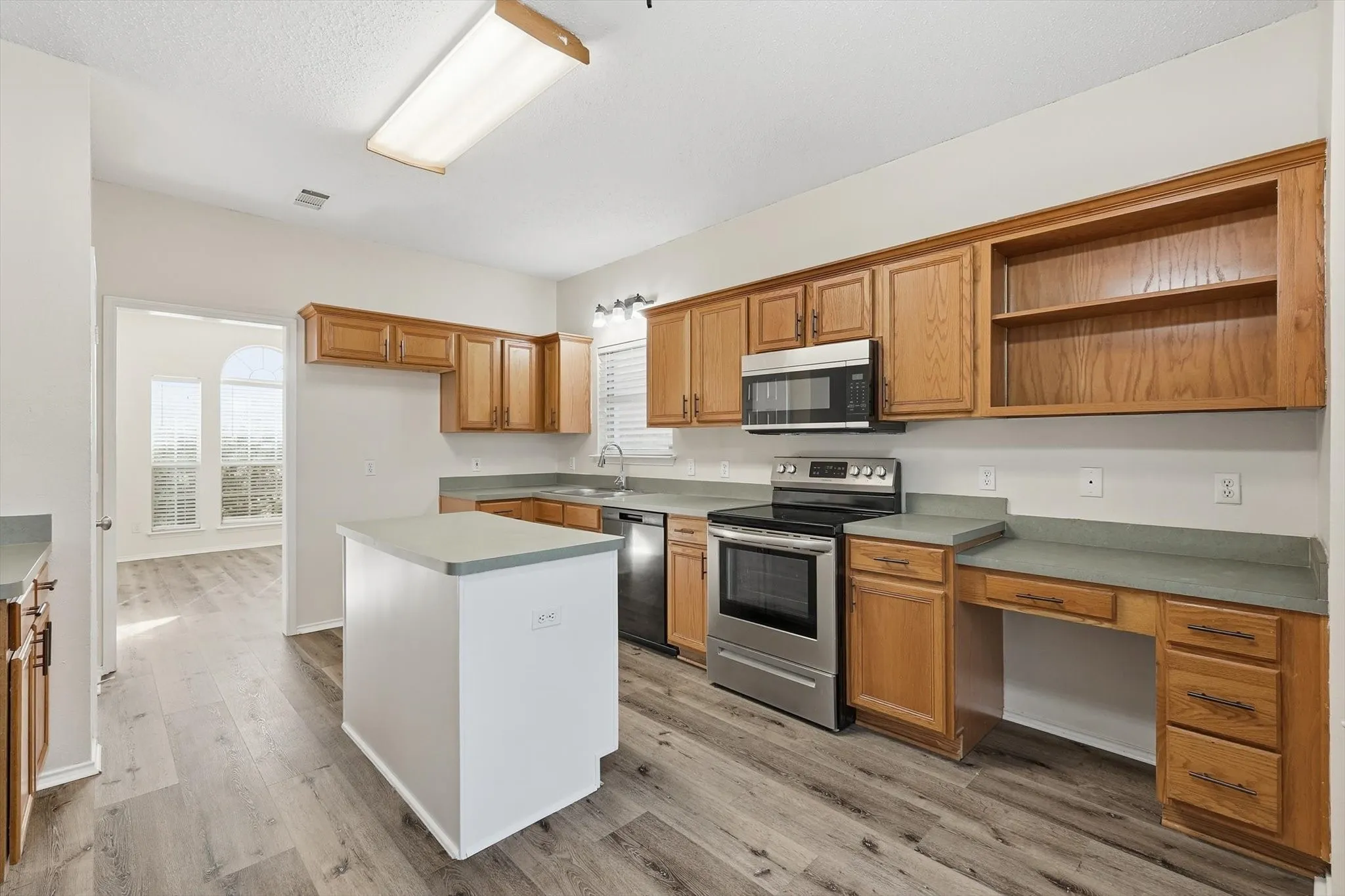 Kitchen featuring stainless steel appliances, a kitchen island, open shelves, wood finish cabinetry, and light countertops