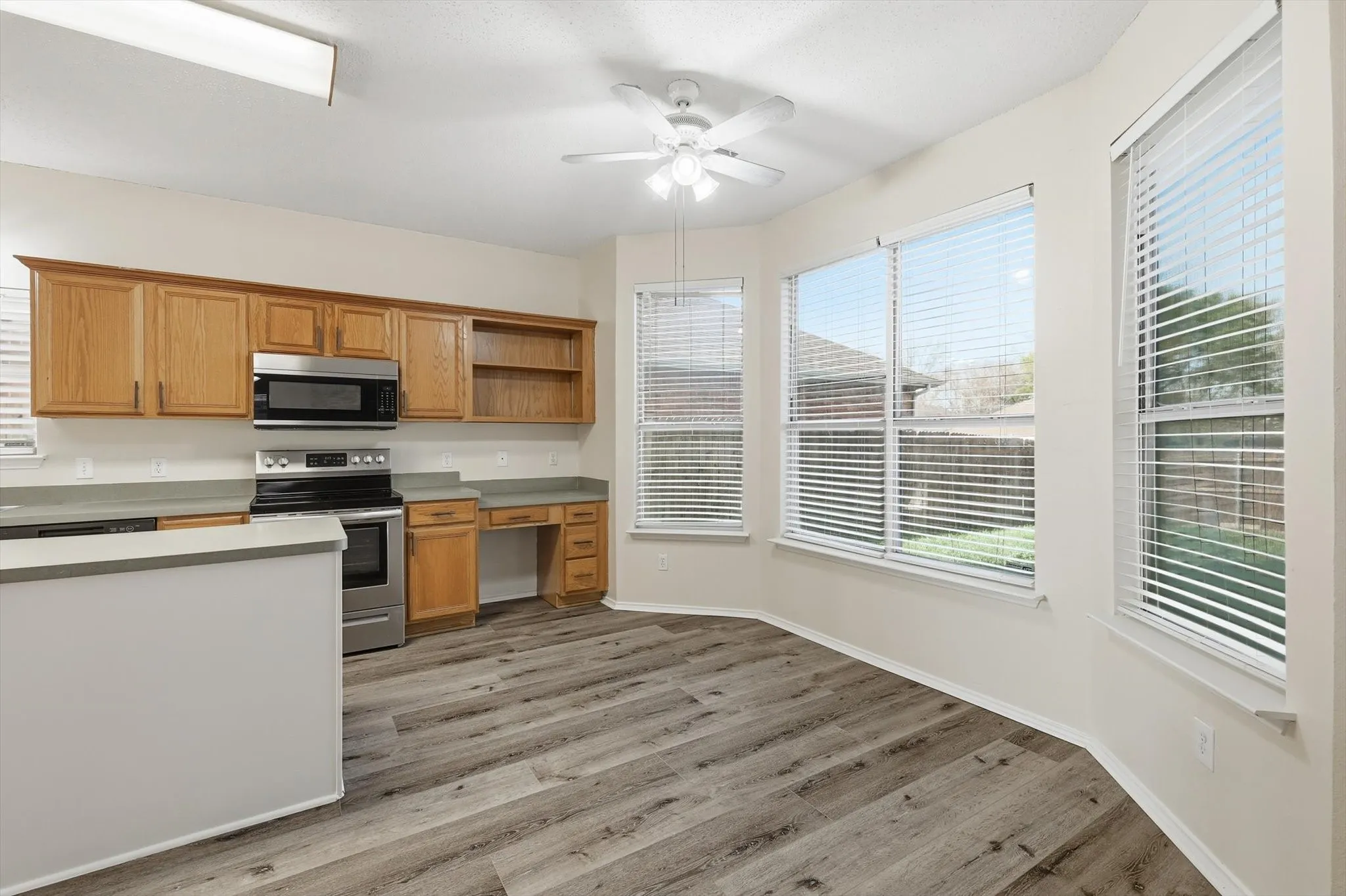 Kitchen with stainless steel appliances, open shelves, a ceiling fan, light countertops, and wood finish cabinets