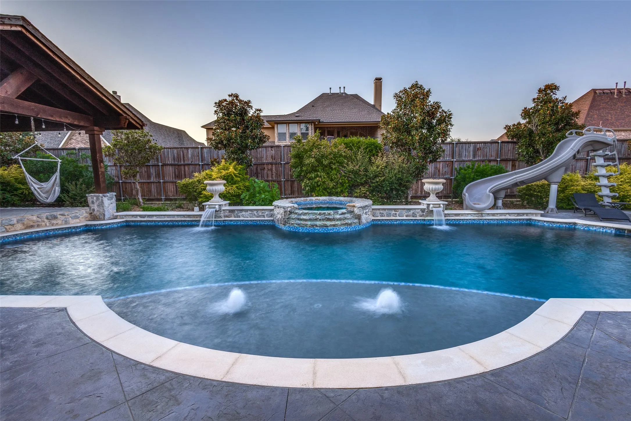 Pool at dusk with a water slide and a pool with connected hot tub