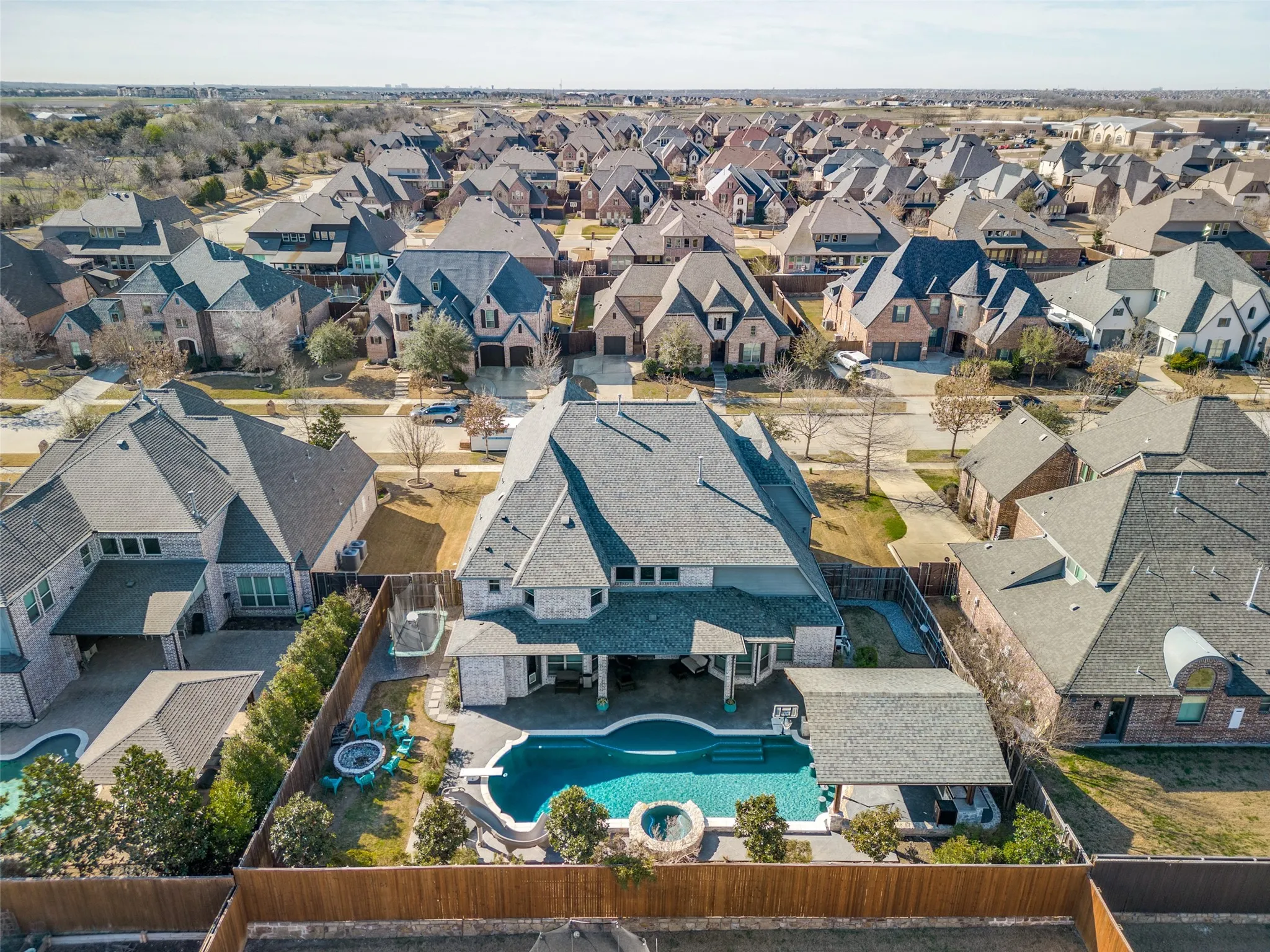 Aerial view of the back of property with the pool, the slide, the diving board, the spa, the tanning bed, the in-pool barstools, and the pergola with the outdoor kitchen.