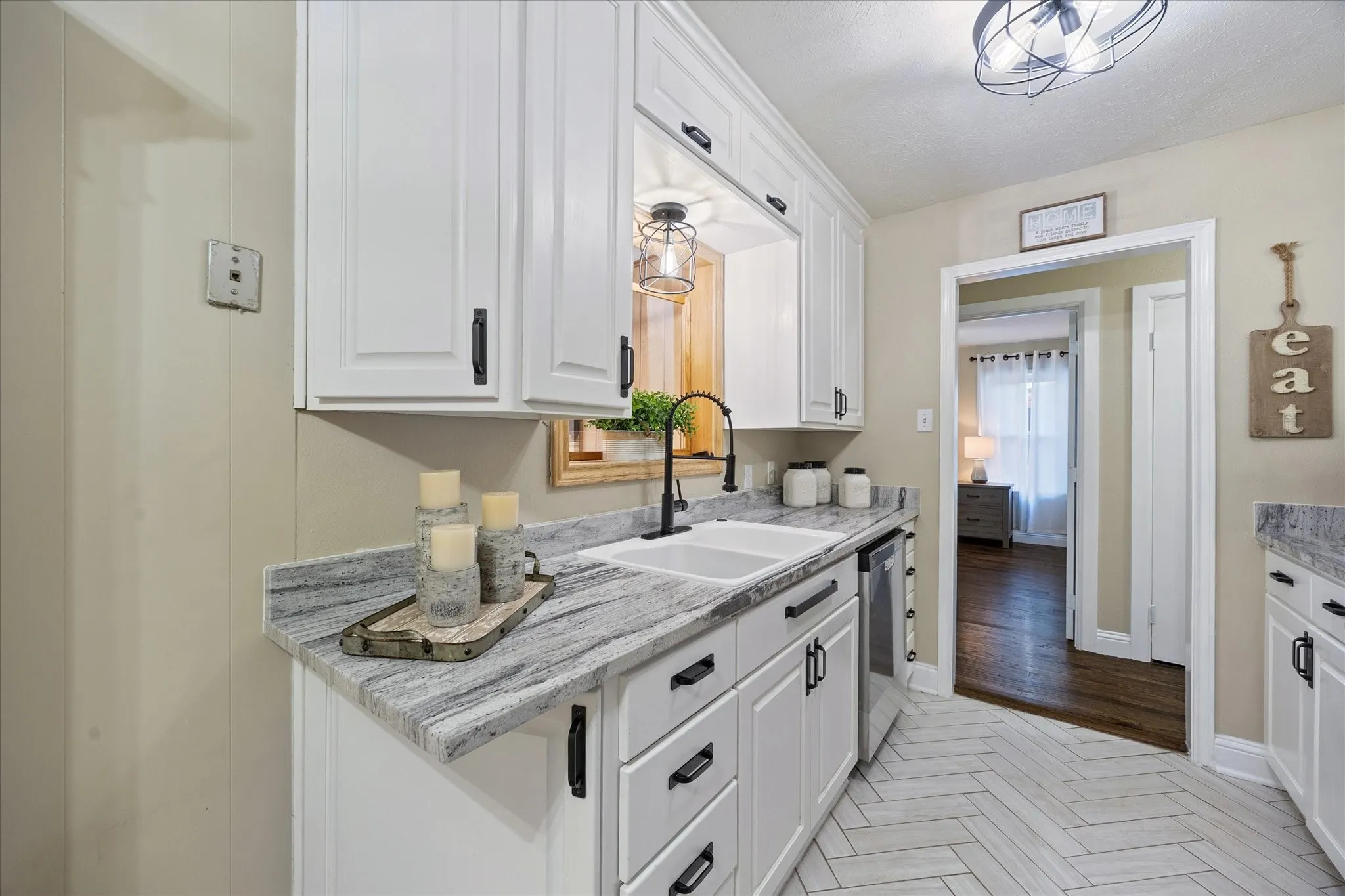 Kitchen featuring white cabinets, parquet floors, light stone countertops, and stainless steel dishwasher