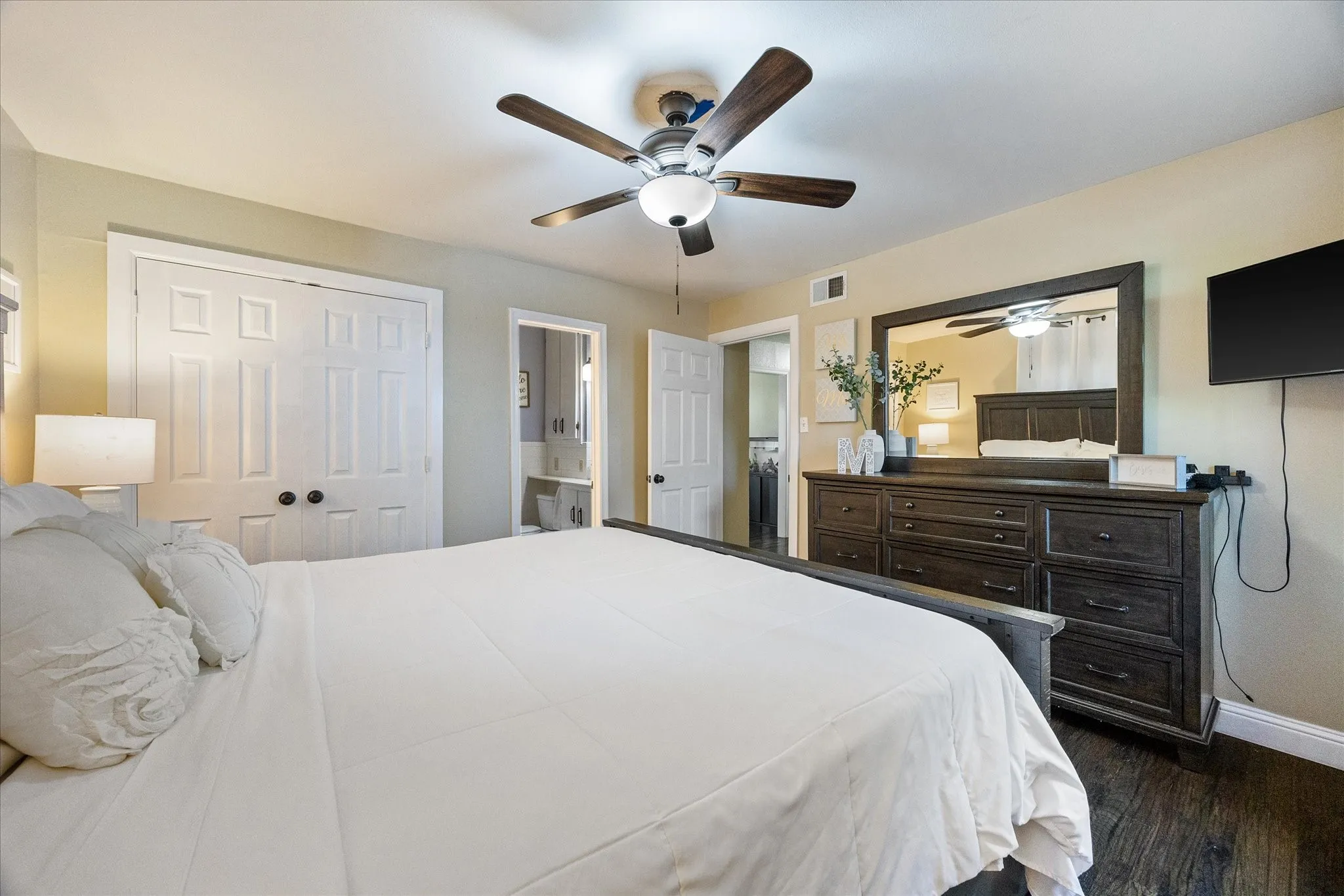 Bedroom featuring a ceiling fan, dark wood-style floors, ensuite bath, and a closet