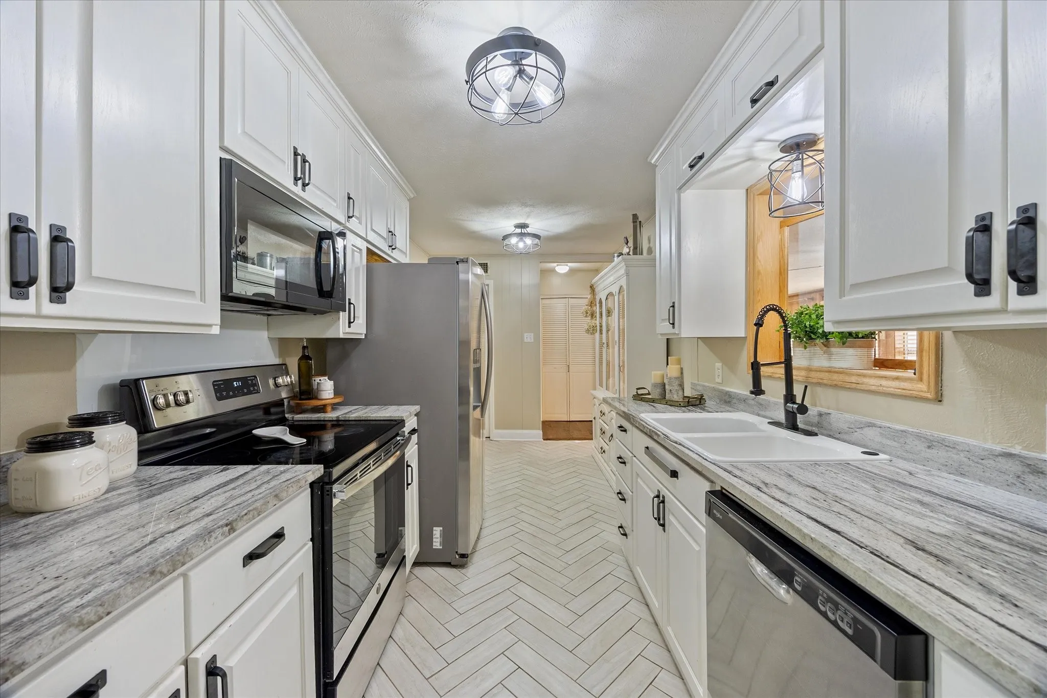 Kitchen featuring stainless steel appliances, white cabinetry, and light stone counters