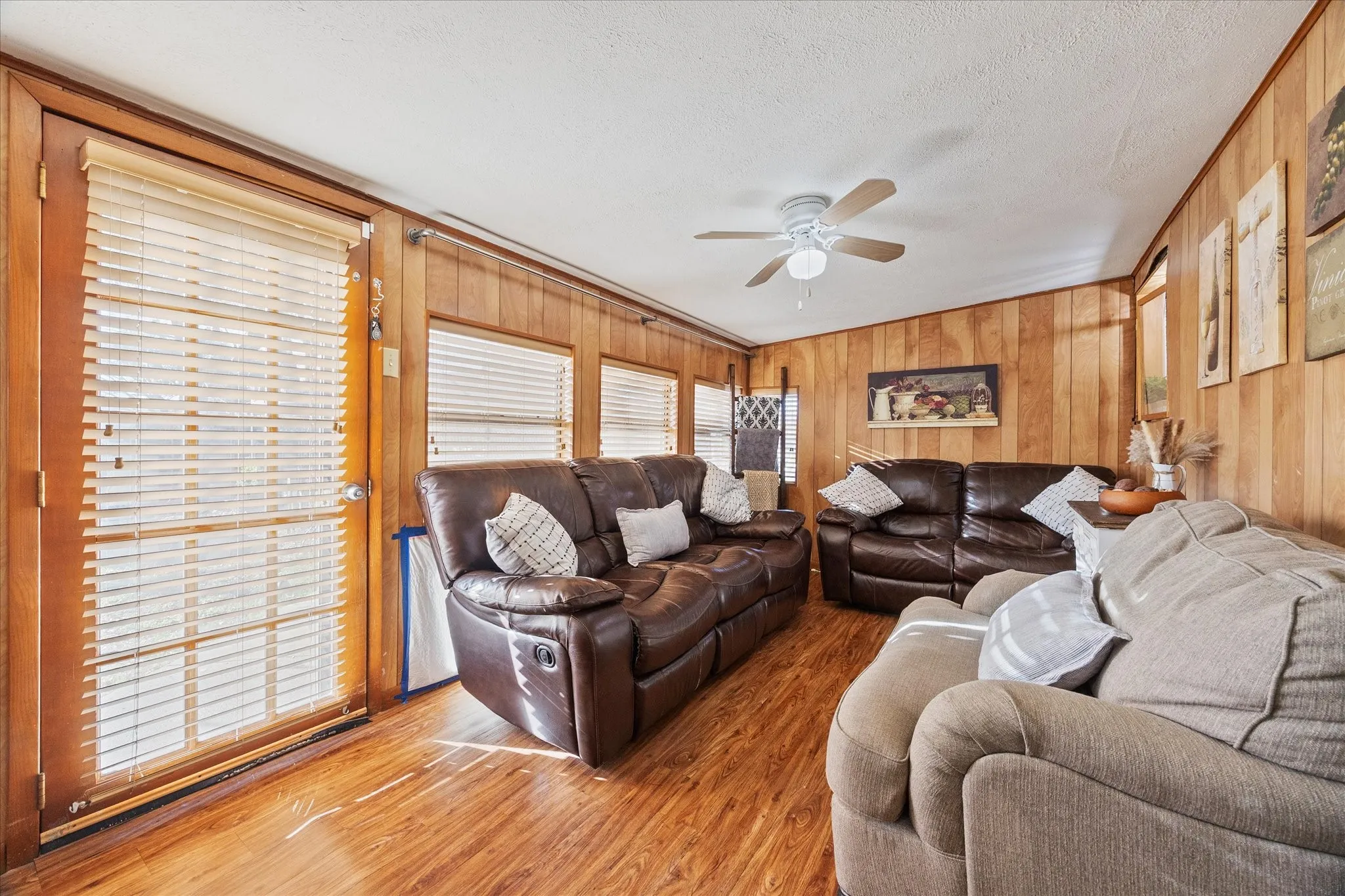 Living room featuring wooden walls, wood finished floors, a ceiling fan, and a textured ceiling