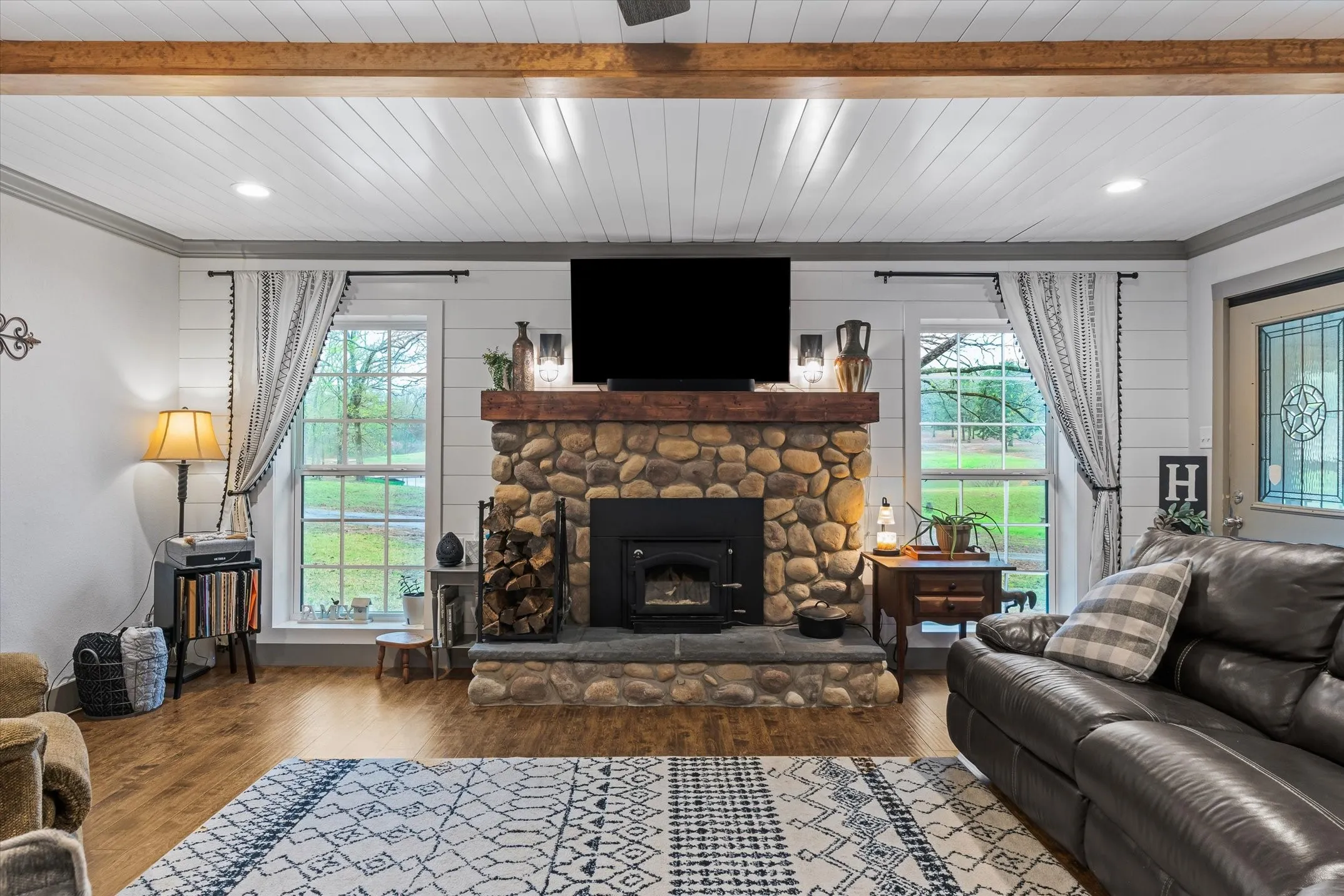 Living room featuring wood finished floors, healthy amount of natural light, a stone fireplace, and wood ceiling
