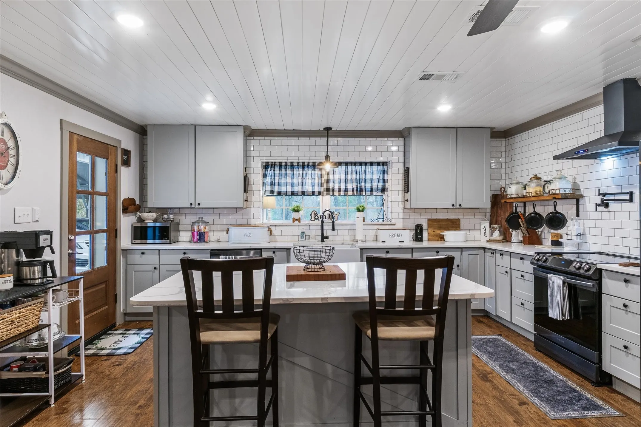Kitchen featuring gray cabinetry, a kitchen island, black electric range oven, a breakfast bar area, and hanging light fixtures