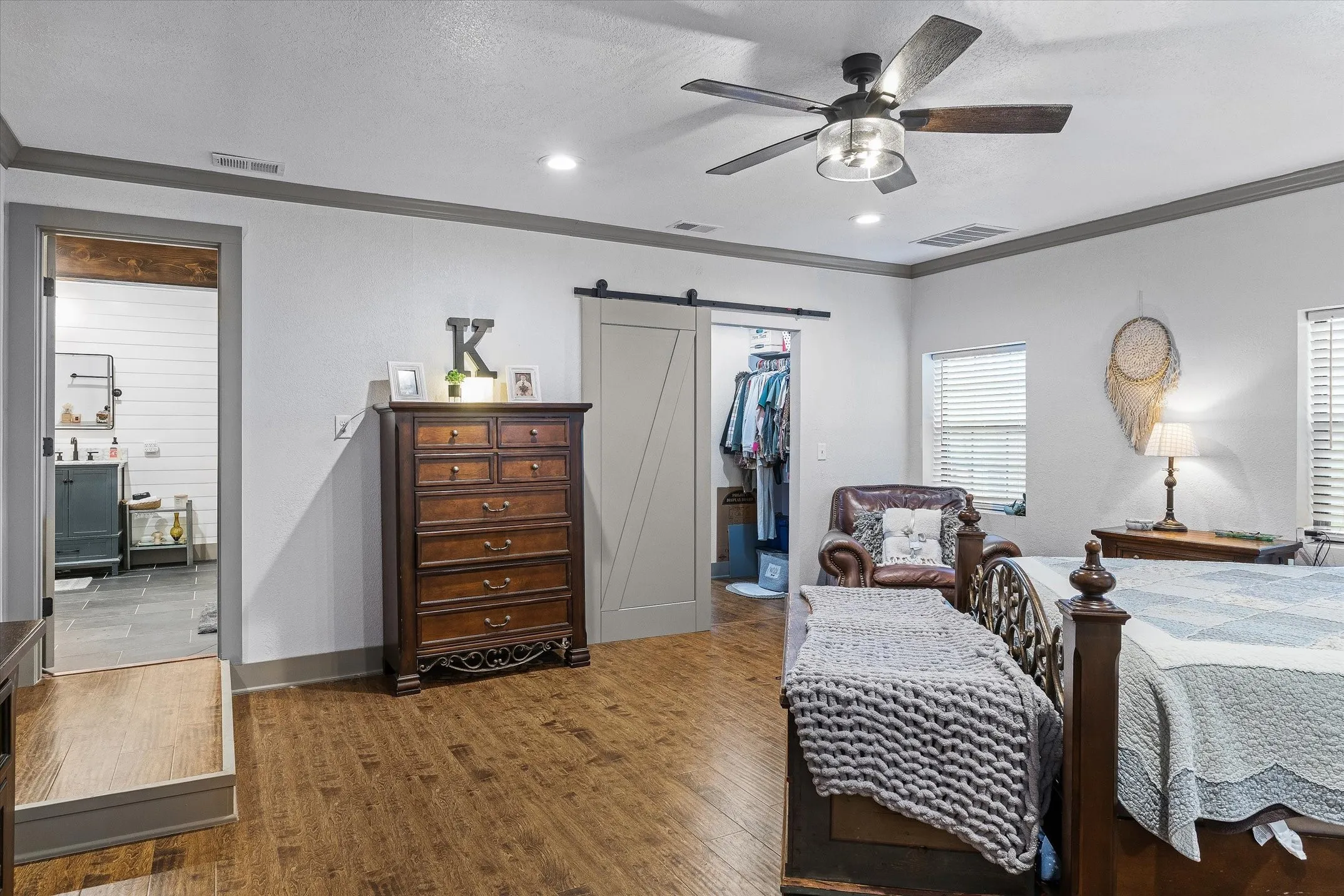 Bedroom featuring crown molding, walk in closet with barn door, ceiling fan, and wood finished floors
