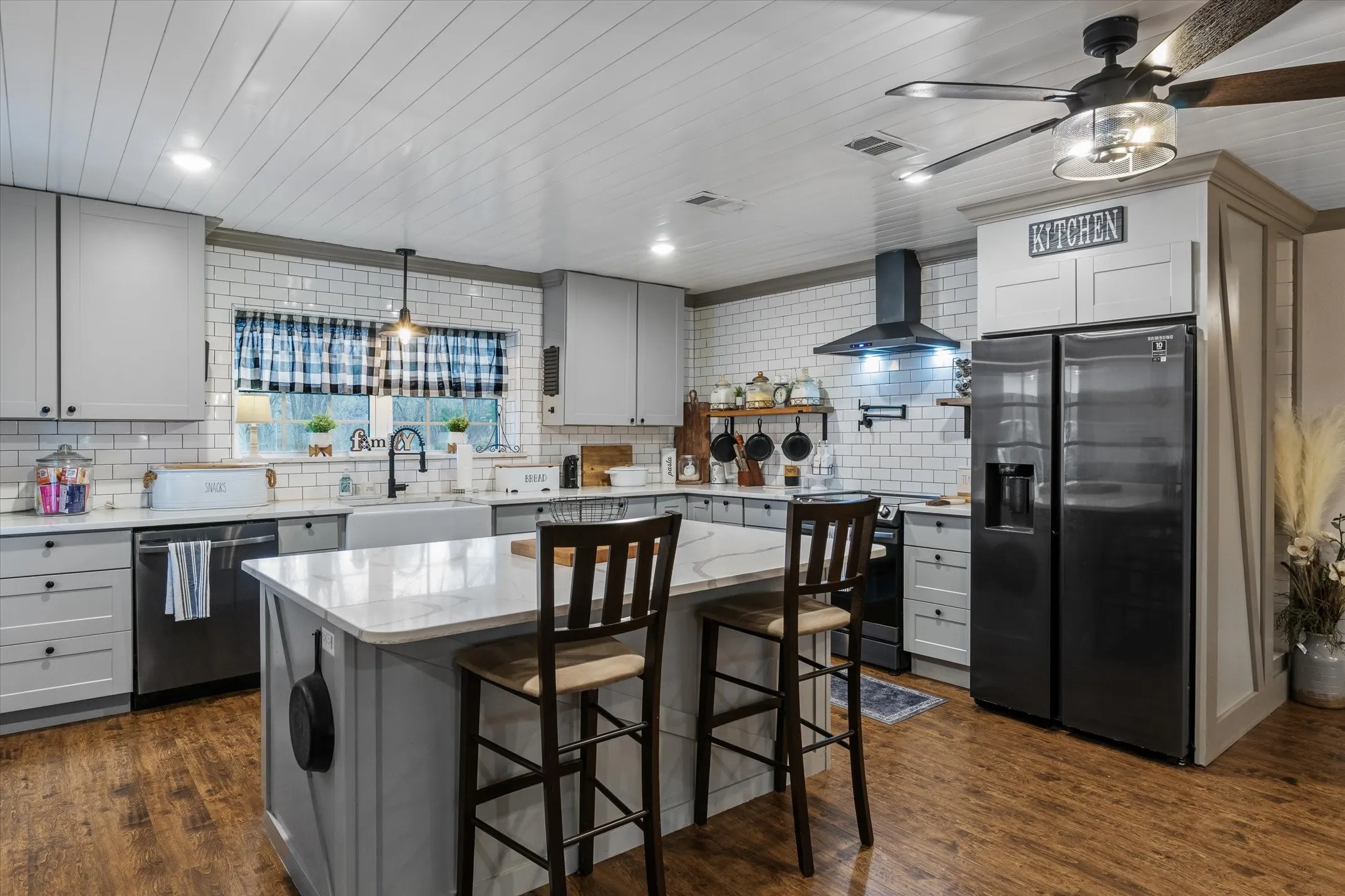 Kitchen with gray cabinets, stainless steel appliances, dark wood-style flooring, a kitchen breakfast bar, and a kitchen island
