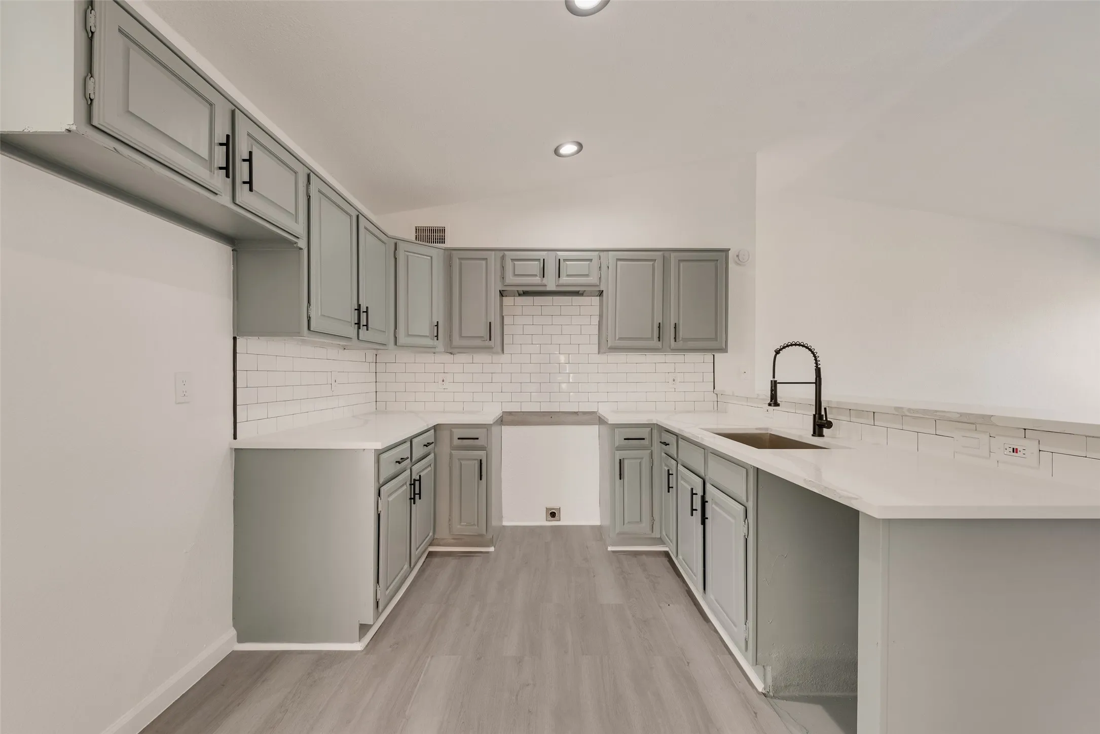 Kitchen with a peninsula, vaulted ceiling, light wood finished floors, light stone countertops, and decorative backsplash