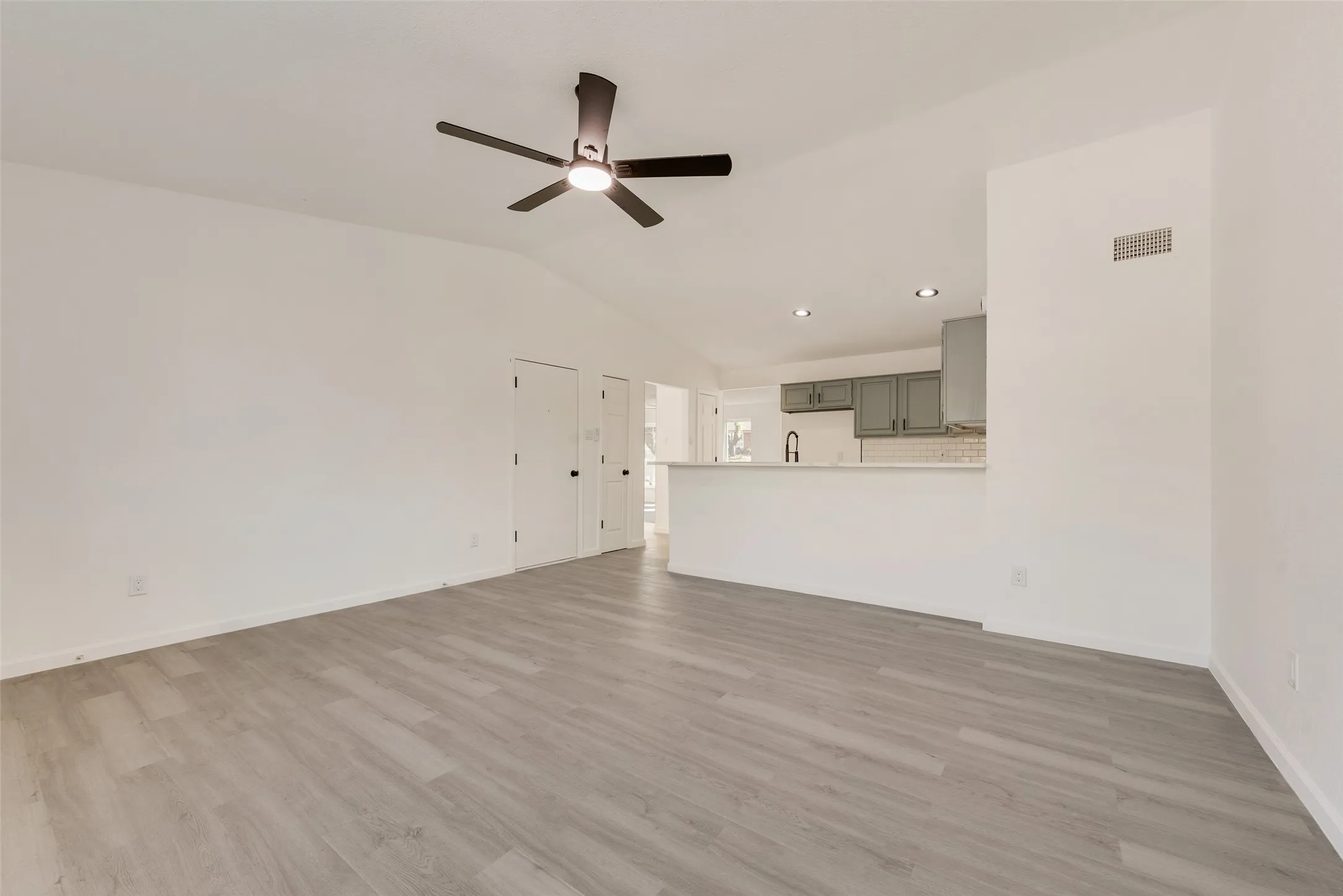 Unfurnished living room featuring a ceiling fan, vaulted ceiling, and light wood-style flooring