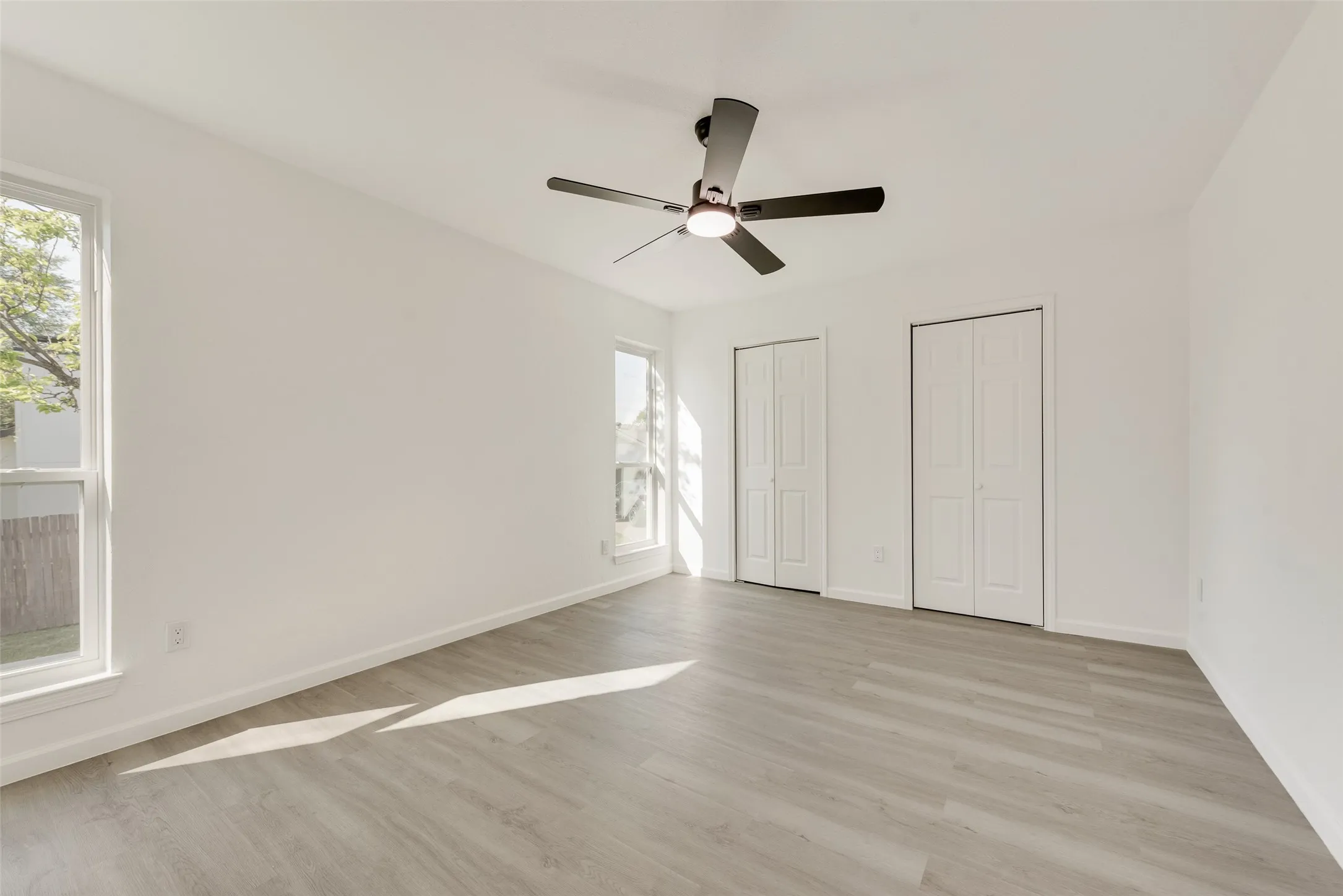 Unfurnished bedroom with multiple closets, light wood-style flooring, and ceiling fan