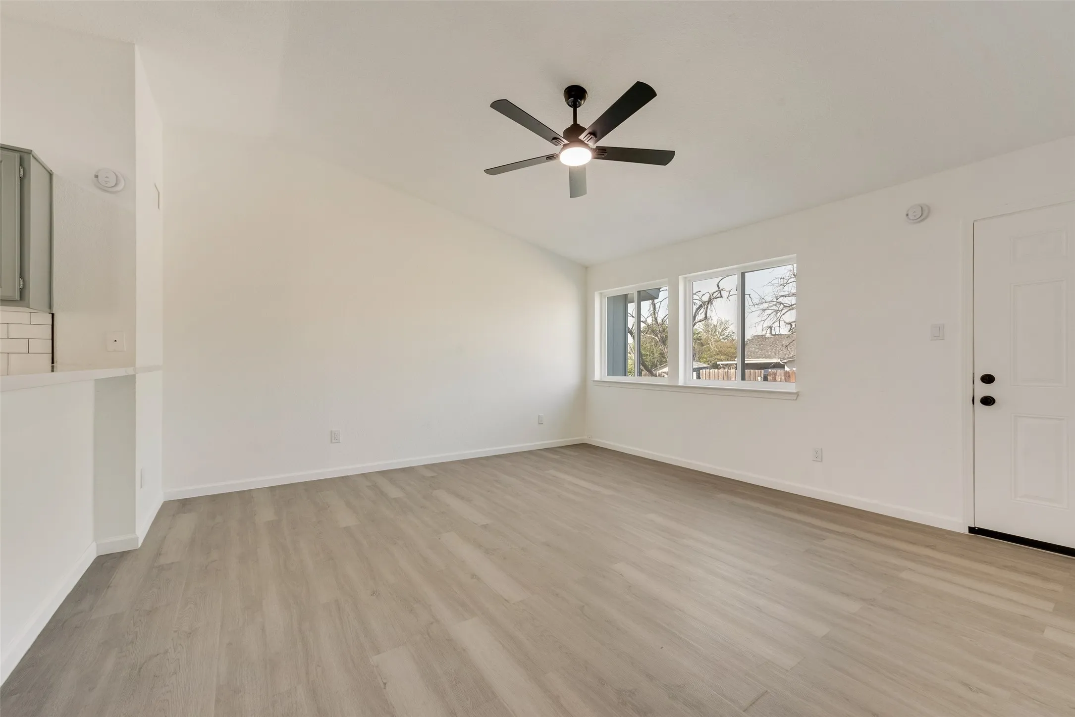 Unfurnished living room featuring light wood-style flooring, lofted ceiling, and a ceiling fan