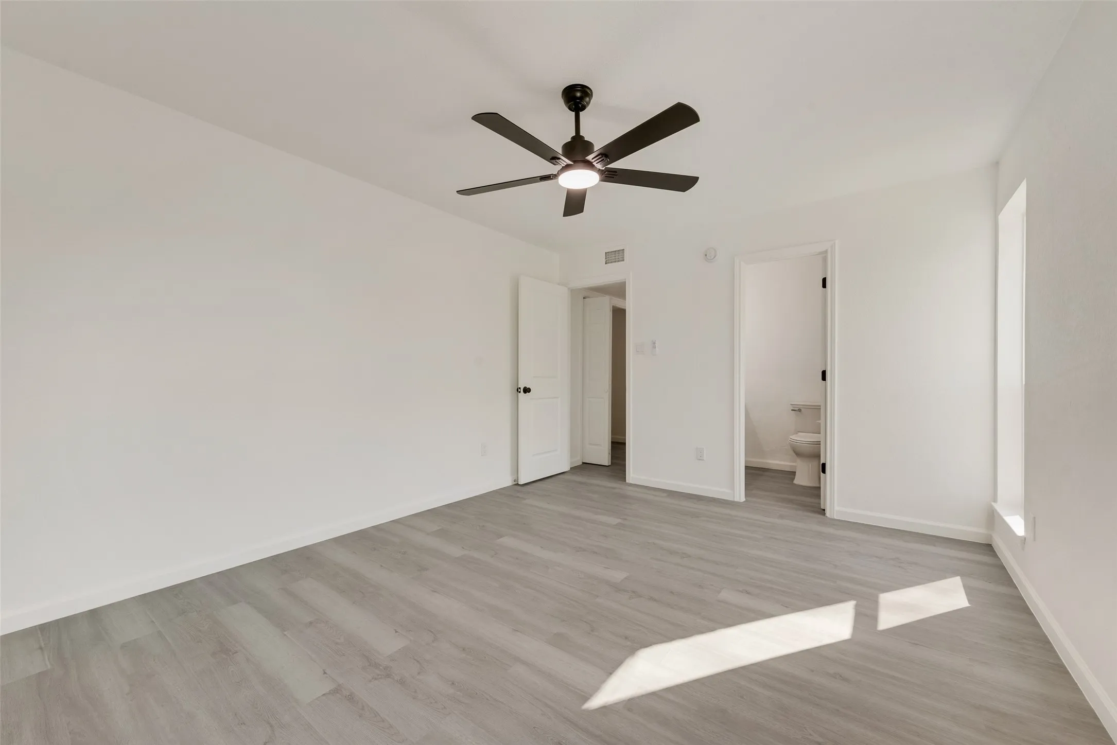 Unfurnished bedroom with ceiling fan, light wood-style flooring, and ensuite bath