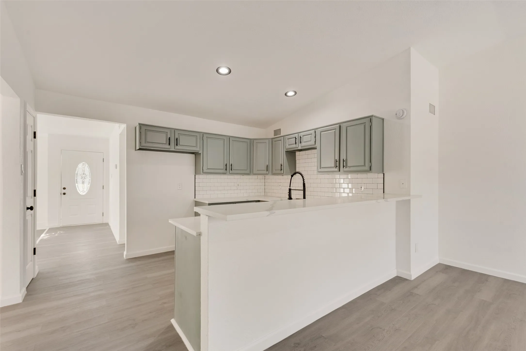 Kitchen featuring a peninsula, lofted ceiling, light wood-style floors, backsplash, and a breakfast bar area