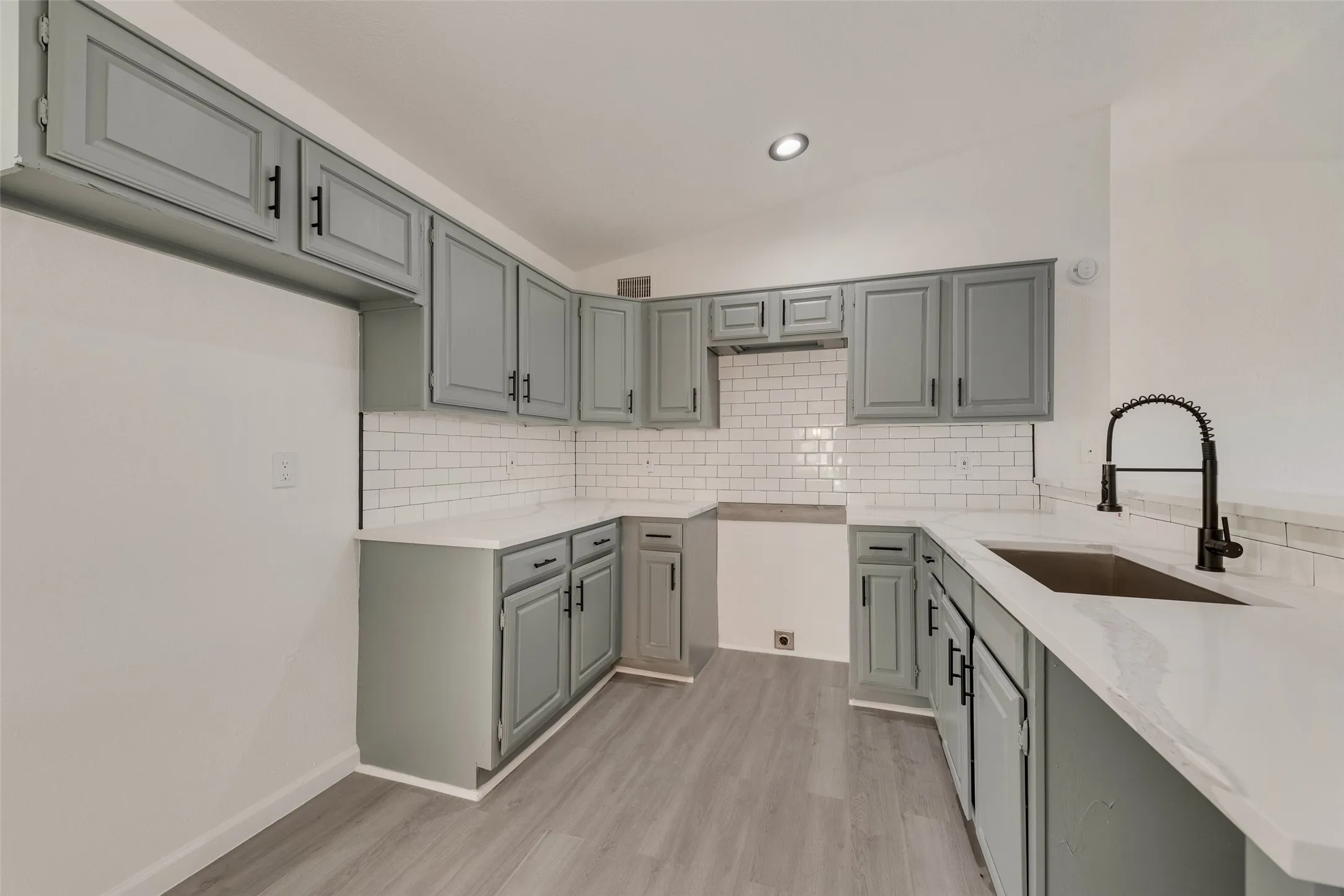Kitchen featuring lofted ceiling, light stone counters, light wood finished floors, a peninsula, and gray cabinetry