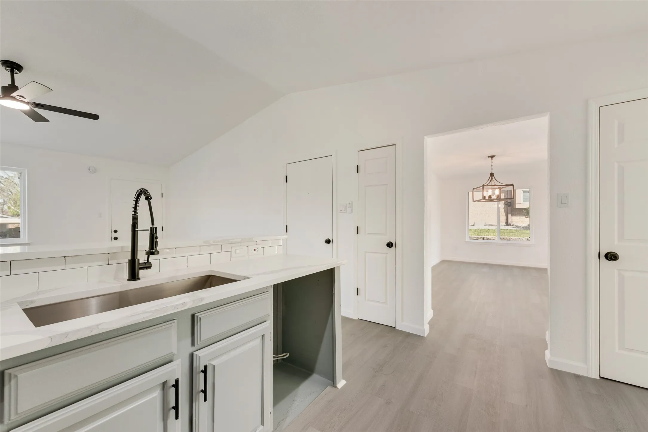 Kitchen with light stone countertops, plenty of natural light, light wood-type flooring, ceiling fan, and vaulted ceiling