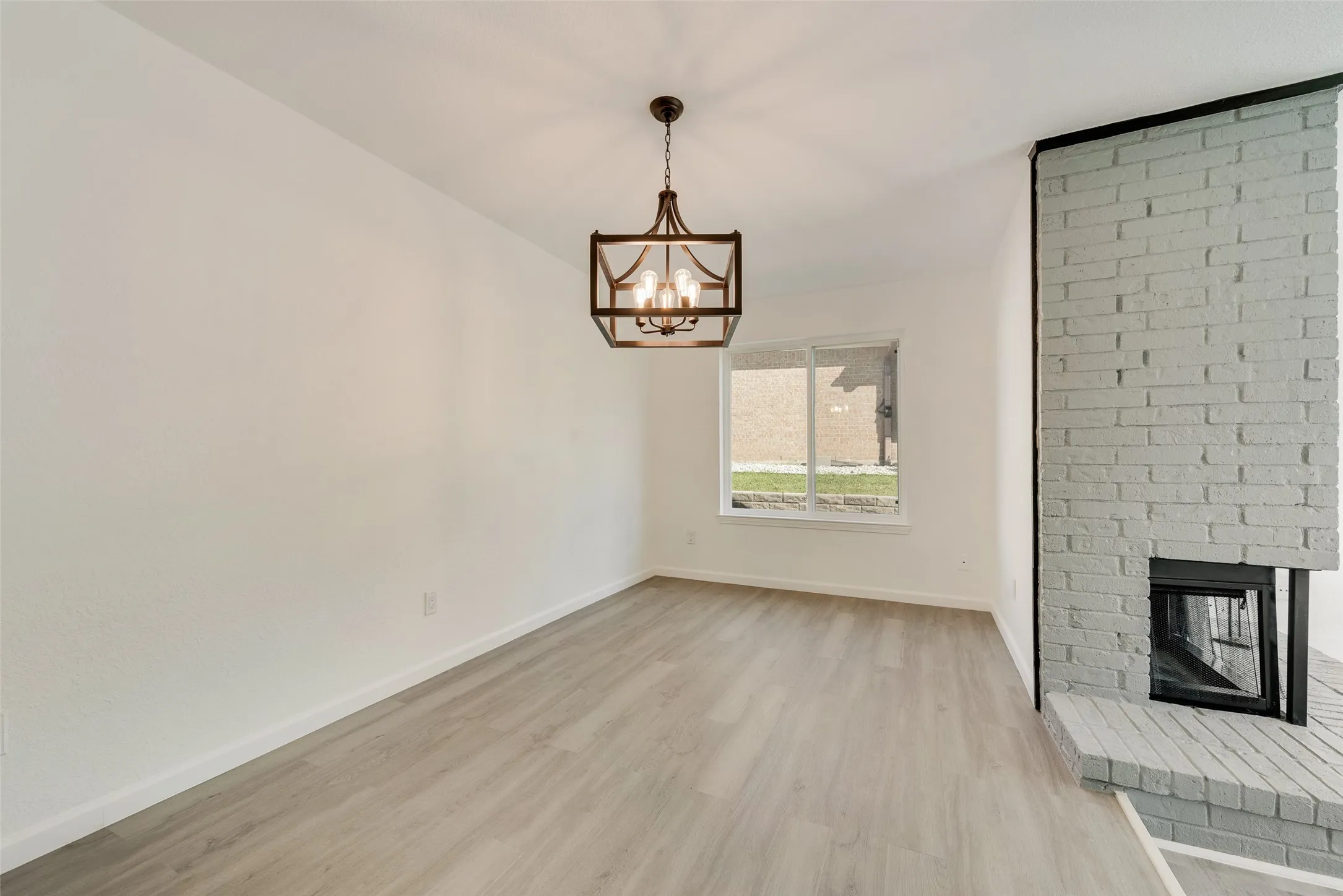 Unfurnished dining room featuring light wood-type flooring, a brick fireplace, and suspended lighting