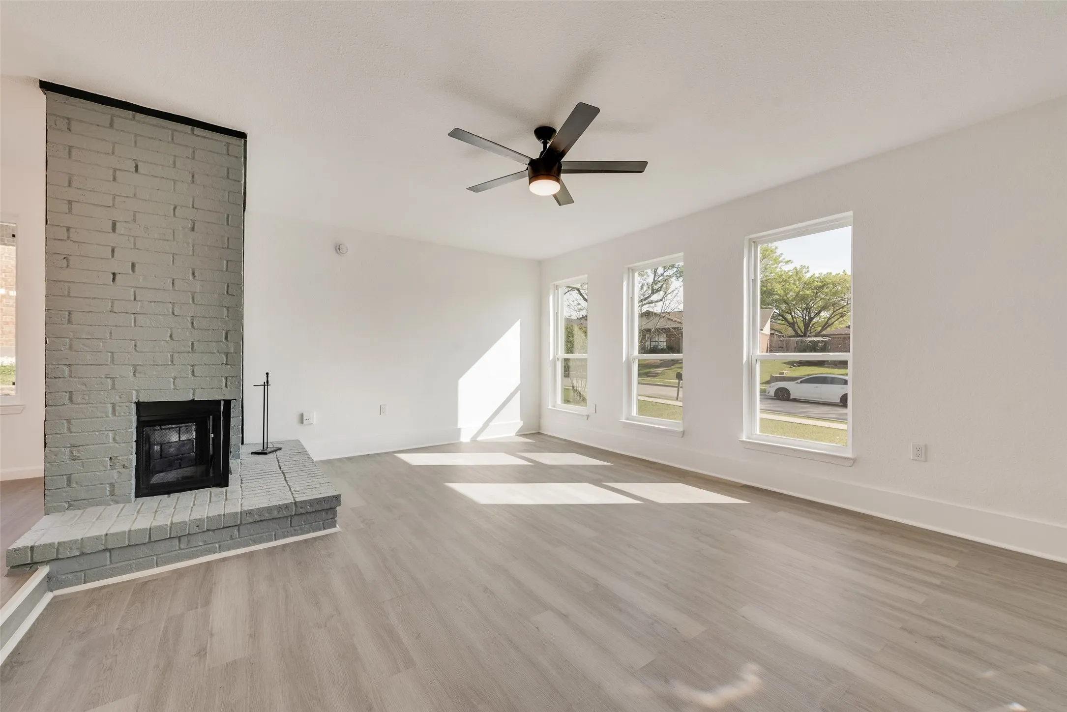 Unfurnished living room featuring a brick fireplace, light wood finished floors, and a ceiling fan