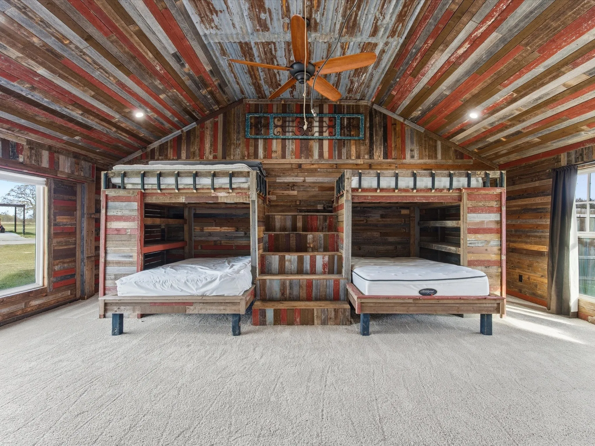 Vaulted ceiling with distressed wood paneling throughout, featuring built-in bunk beds with integrated steps, soft pile carpet, and natural light from multiple windows