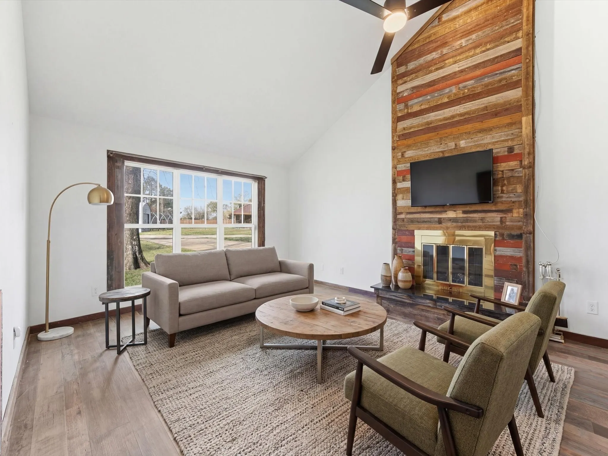 Vaulted ceiling with a contemporary ceiling fan, prominent fireplace featuring a rustic wood-finish facade, wide plank wood-finish flooring, and built-in cabinetry with a countertop