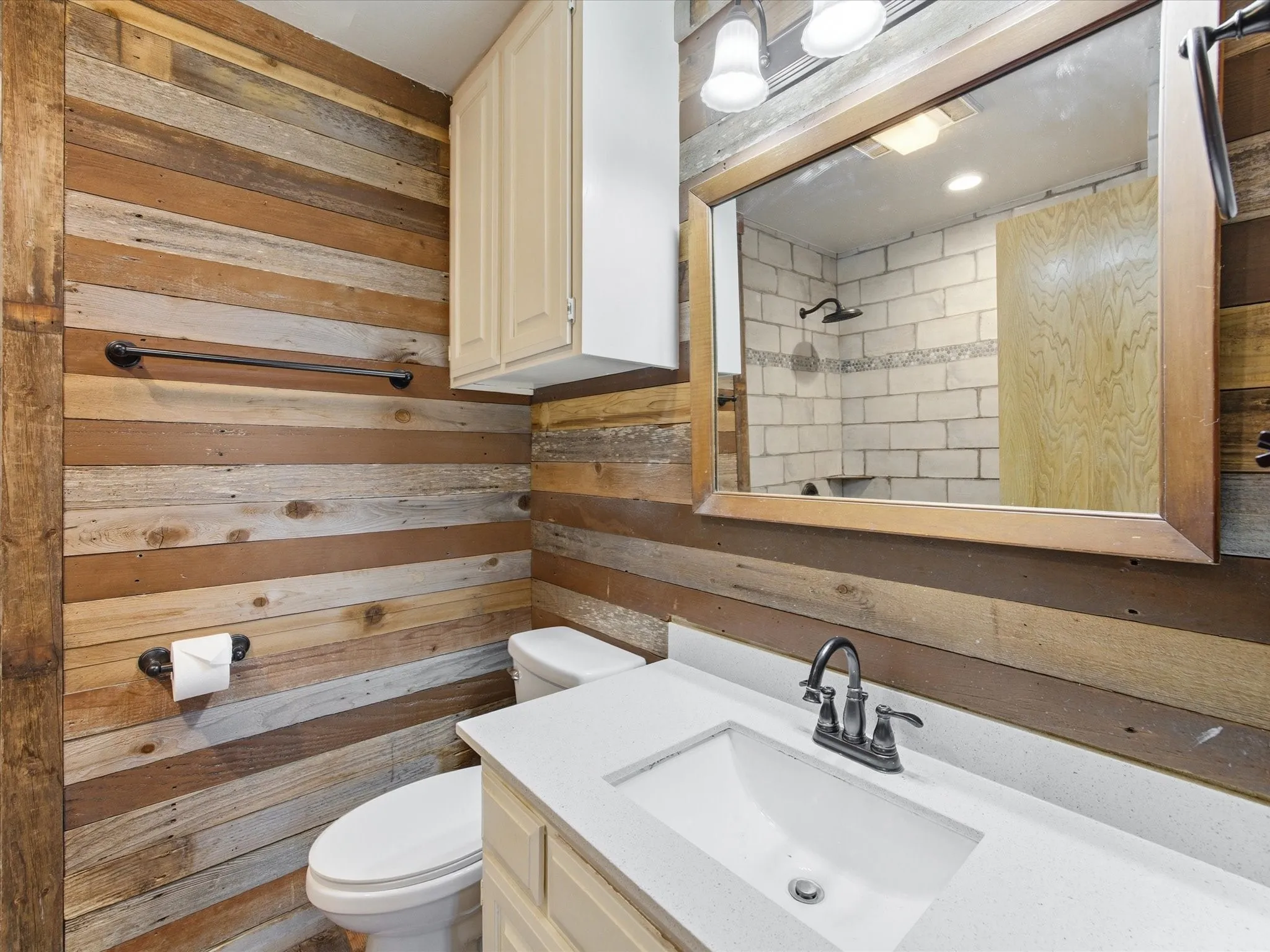 Bathroom featuring varied wood-plank walls, a white countertop vanity with an integrated sink, and a rectangular mirror with a wood-finish frame