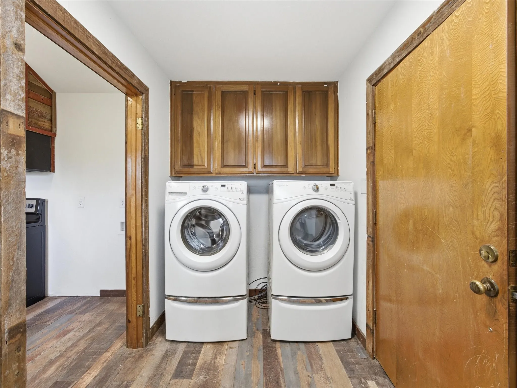 Dedicated laundry area featuring wood-finish flooring, overhead wood cabinetry, and a full-size washer and dryer