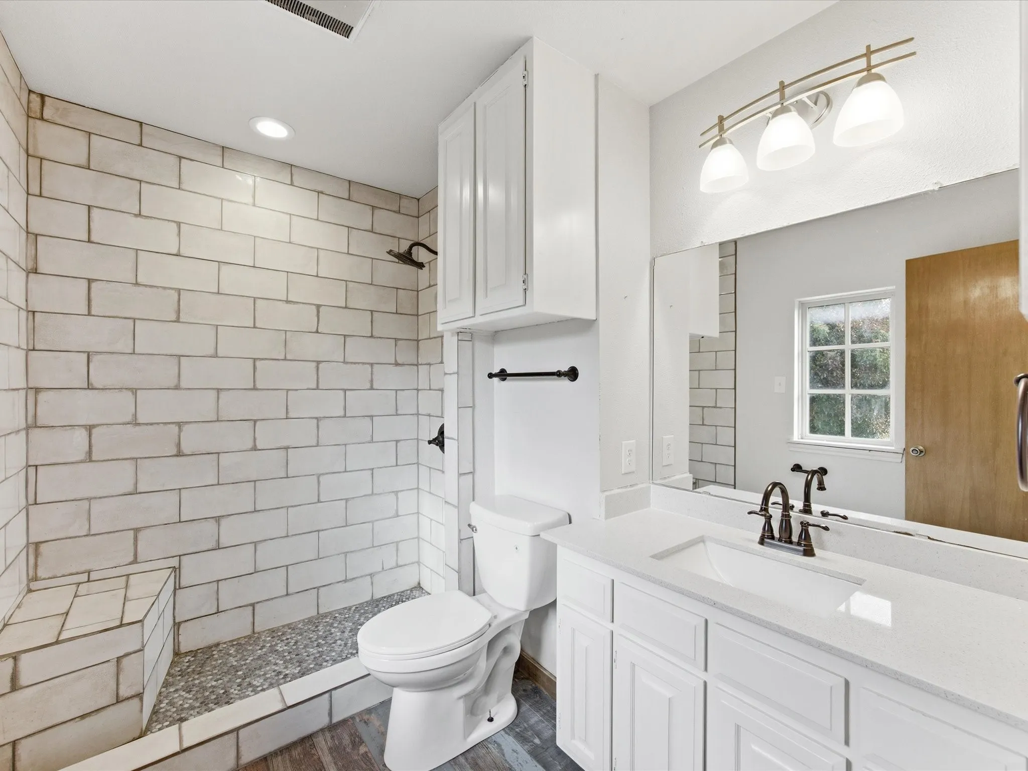 Contemporary bathroom featuring a walk-in shower with subway tile, pebble flooring, and a built-in bench