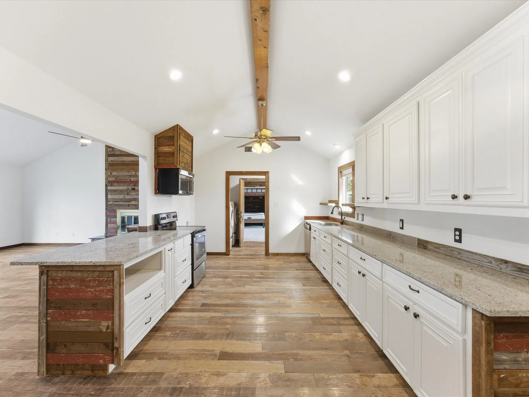 Open-concept living space featuring wood-finish flooring, vaulted ceilings with exposed wood beams, and a ceiling fan