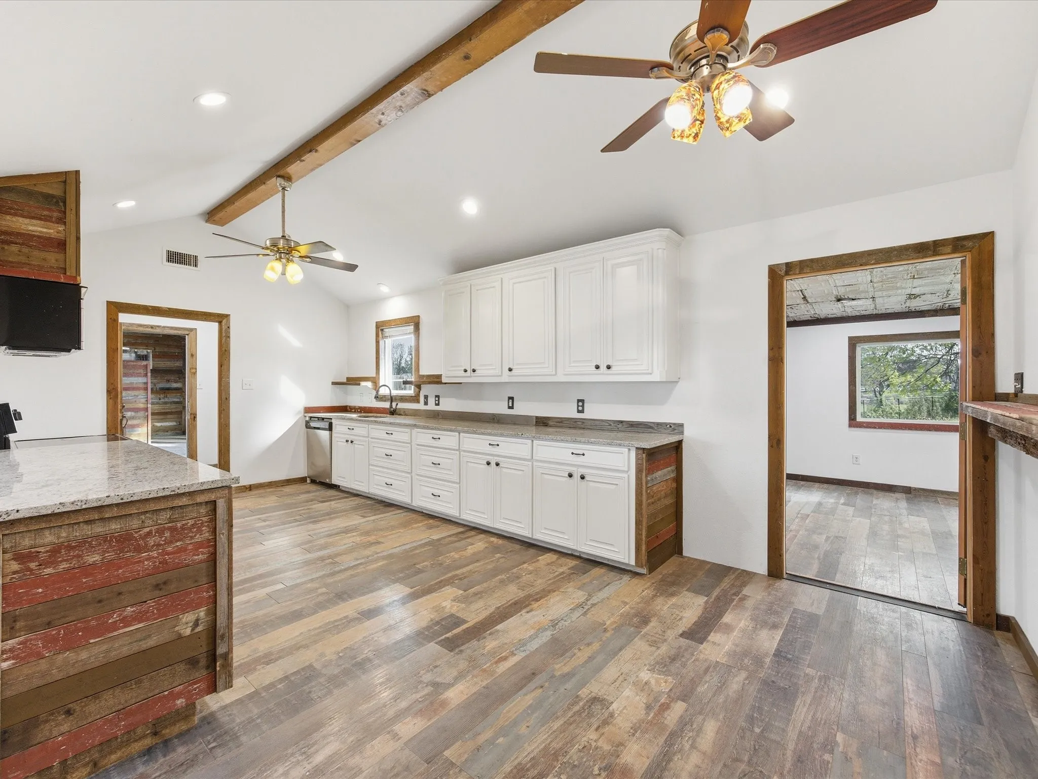 Kitchen featuring white upper and lower cabinetry, stainless steel dishwasher, ample countertop space, and wood-finish flooring