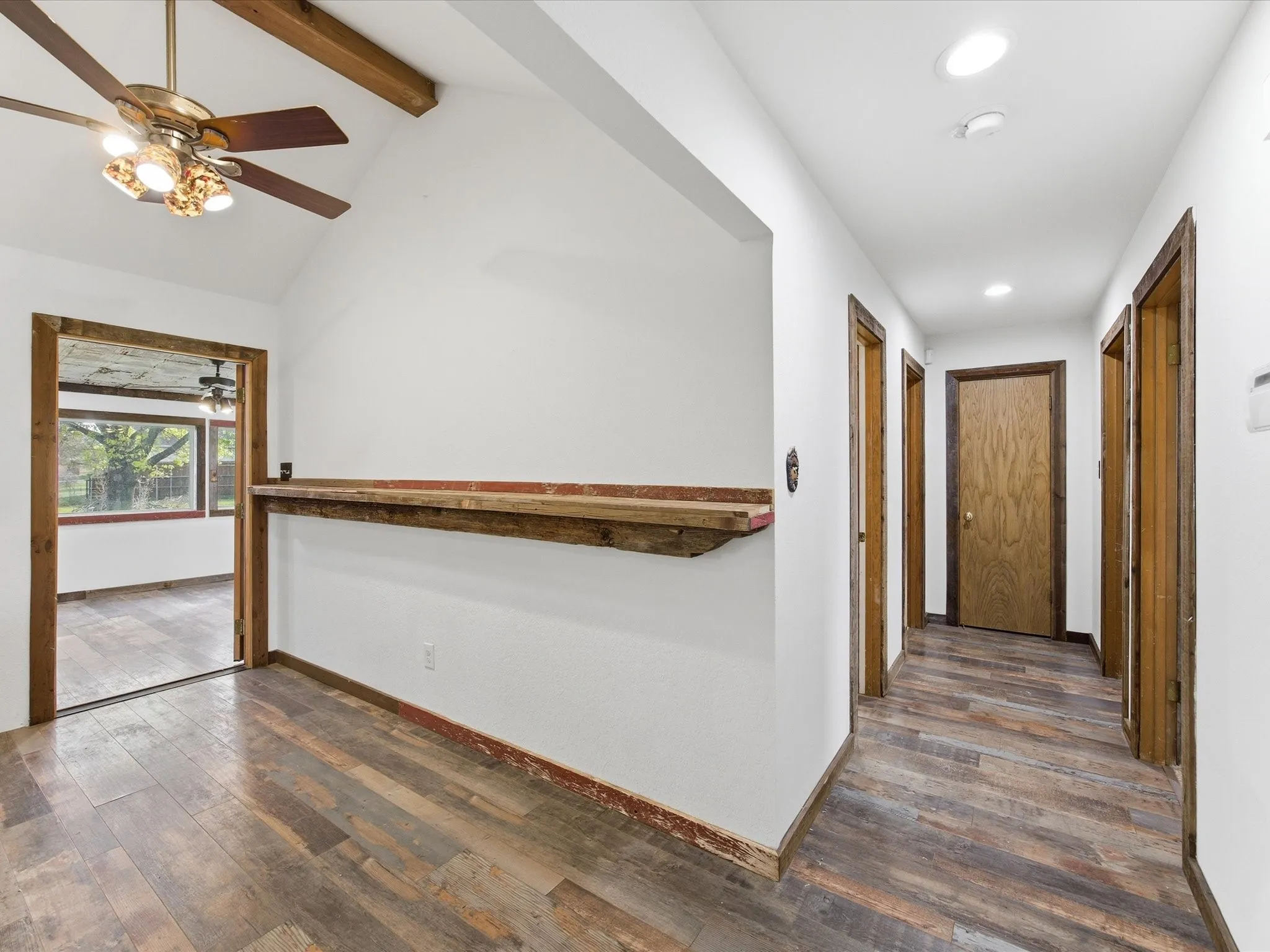 Kitchen featuring white upper and lower cabinetry, stainless steel dishwasher, ample countertop space, and wood-finish flooring
