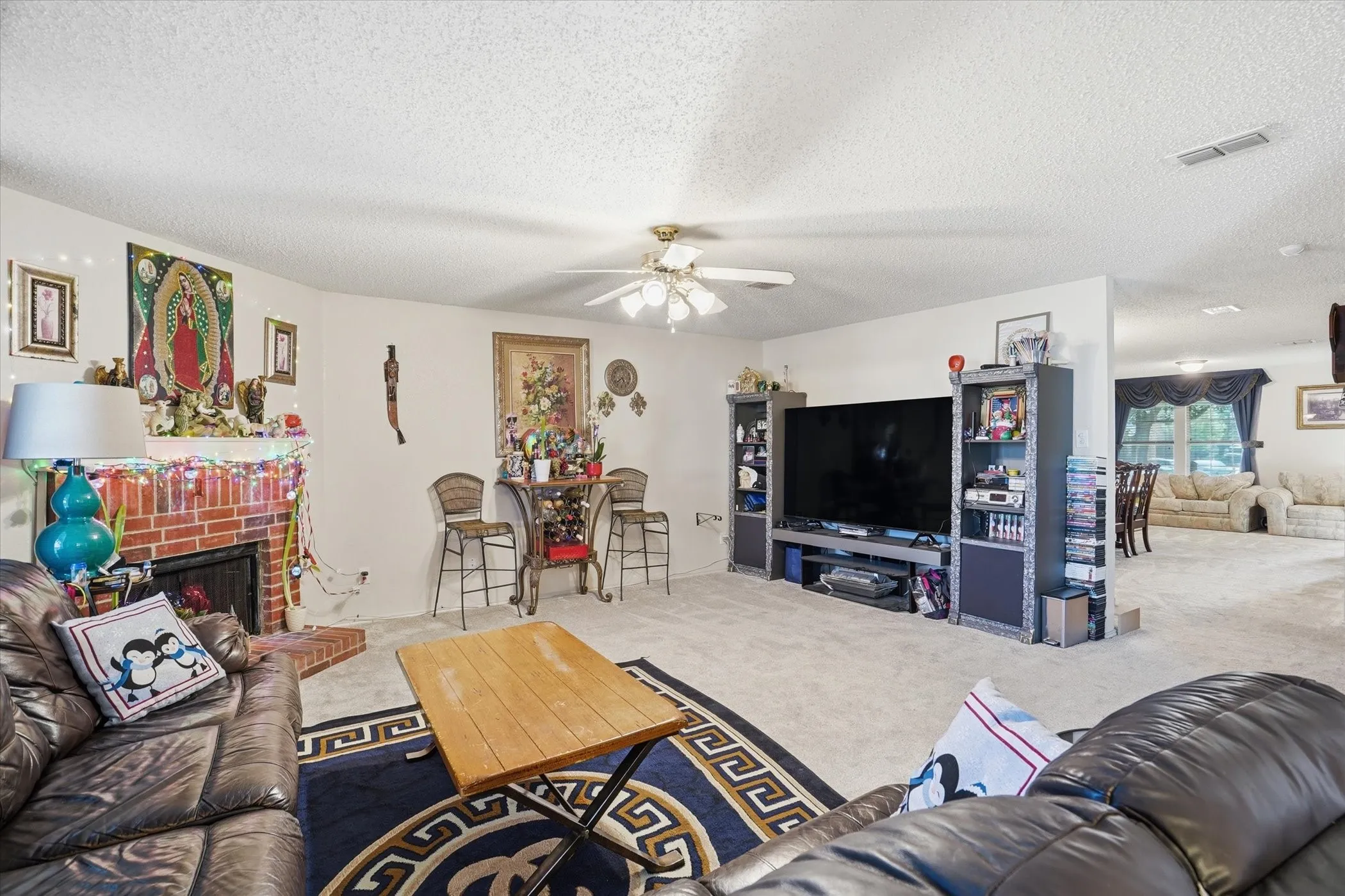 Carpeted living area featuring a ceiling fan, a fireplace, and a textured ceiling