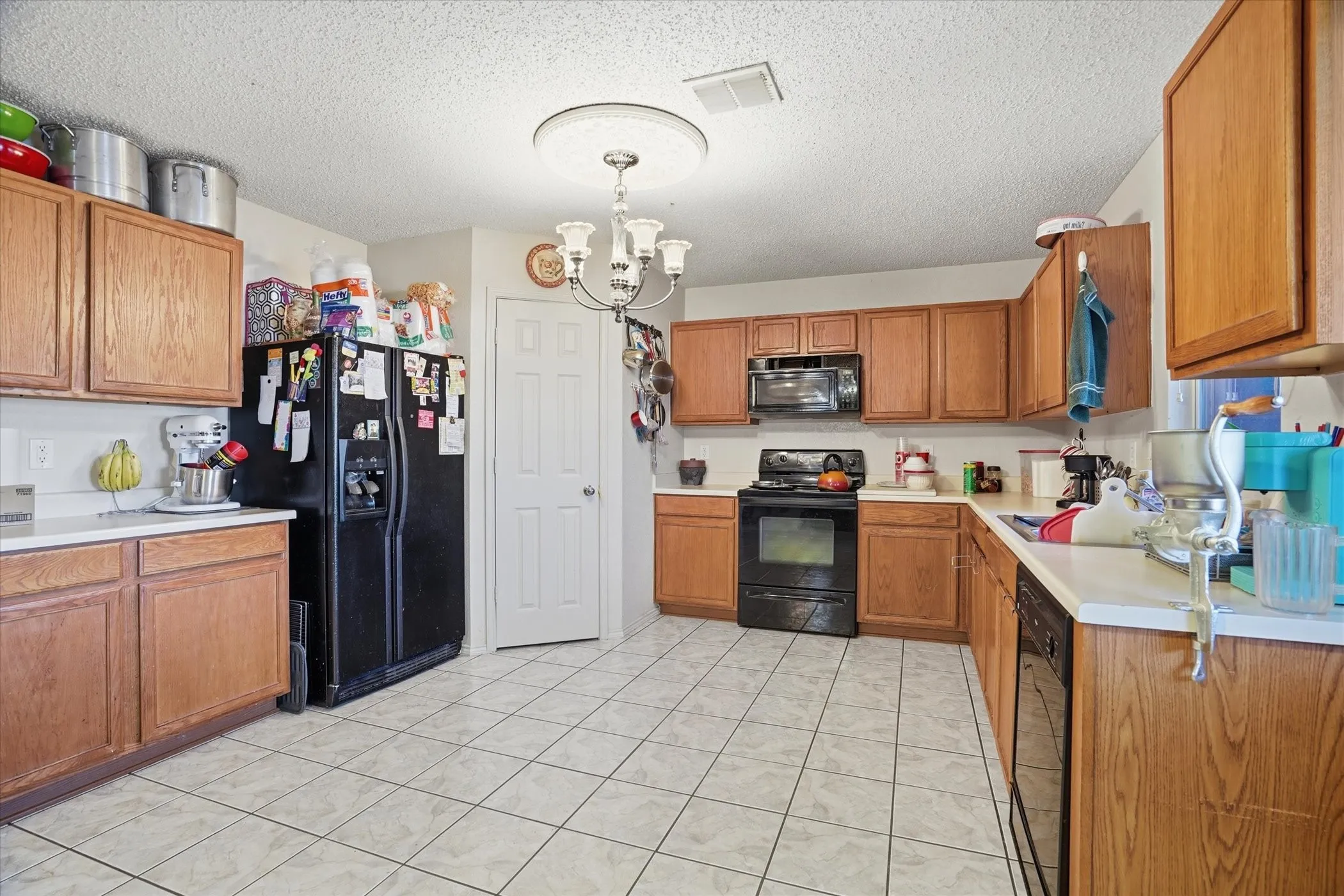 Kitchen featuring hanging lights, light countertops, wood finish cabinets, black appliances, and a textured ceiling