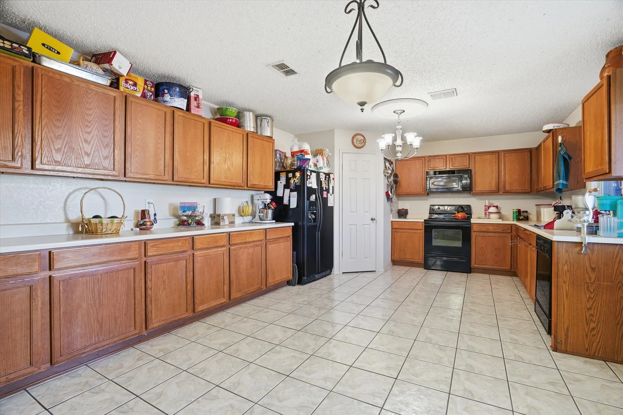 Kitchen featuring light countertops, wood finish cabinetry, black appliances, a textured ceiling, and suspended lighting