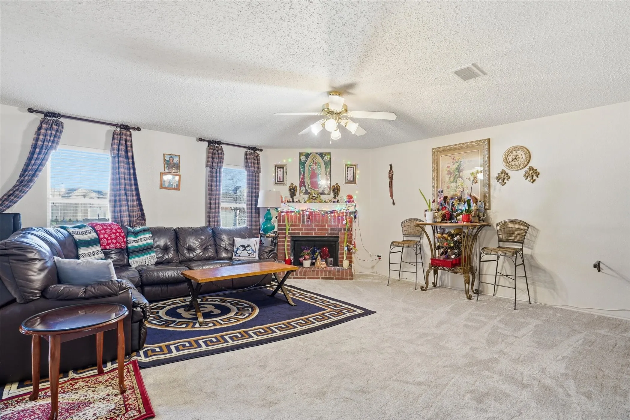 Living area with carpet flooring, a ceiling fan, a brick fireplace, and a textured ceiling