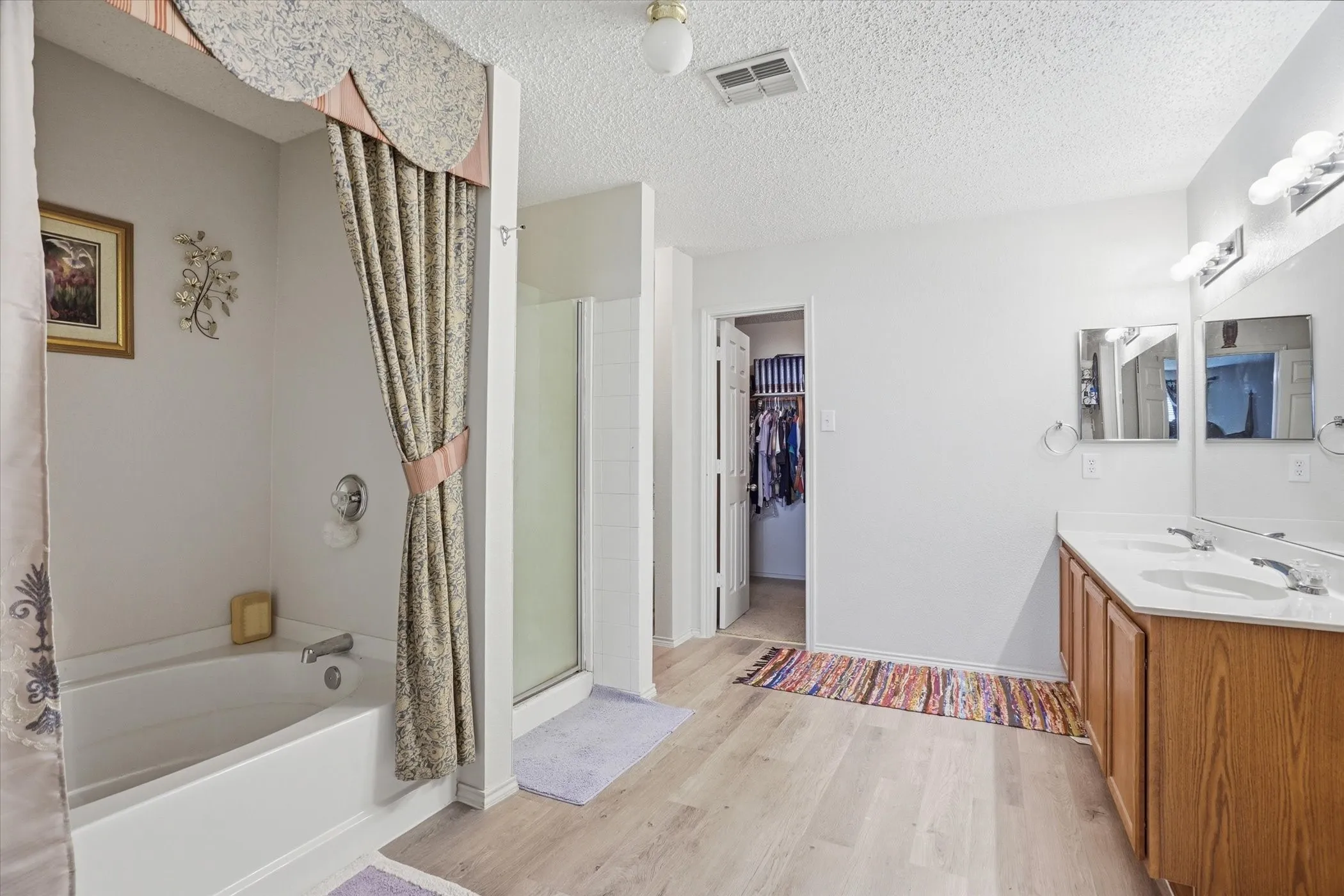 Full bath with a bath, double vanity, a spacious closet, a shower stall, and light wood-style flooring