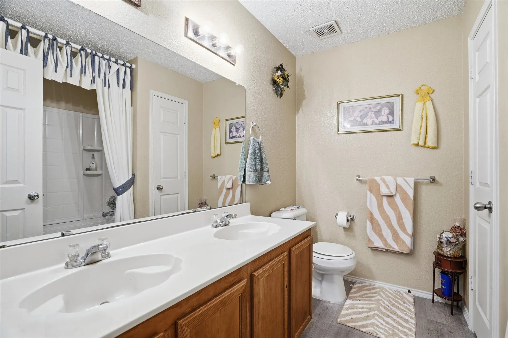 Full bathroom with double vanity, a textured ceiling, a shower with curtain, and light wood-style floors