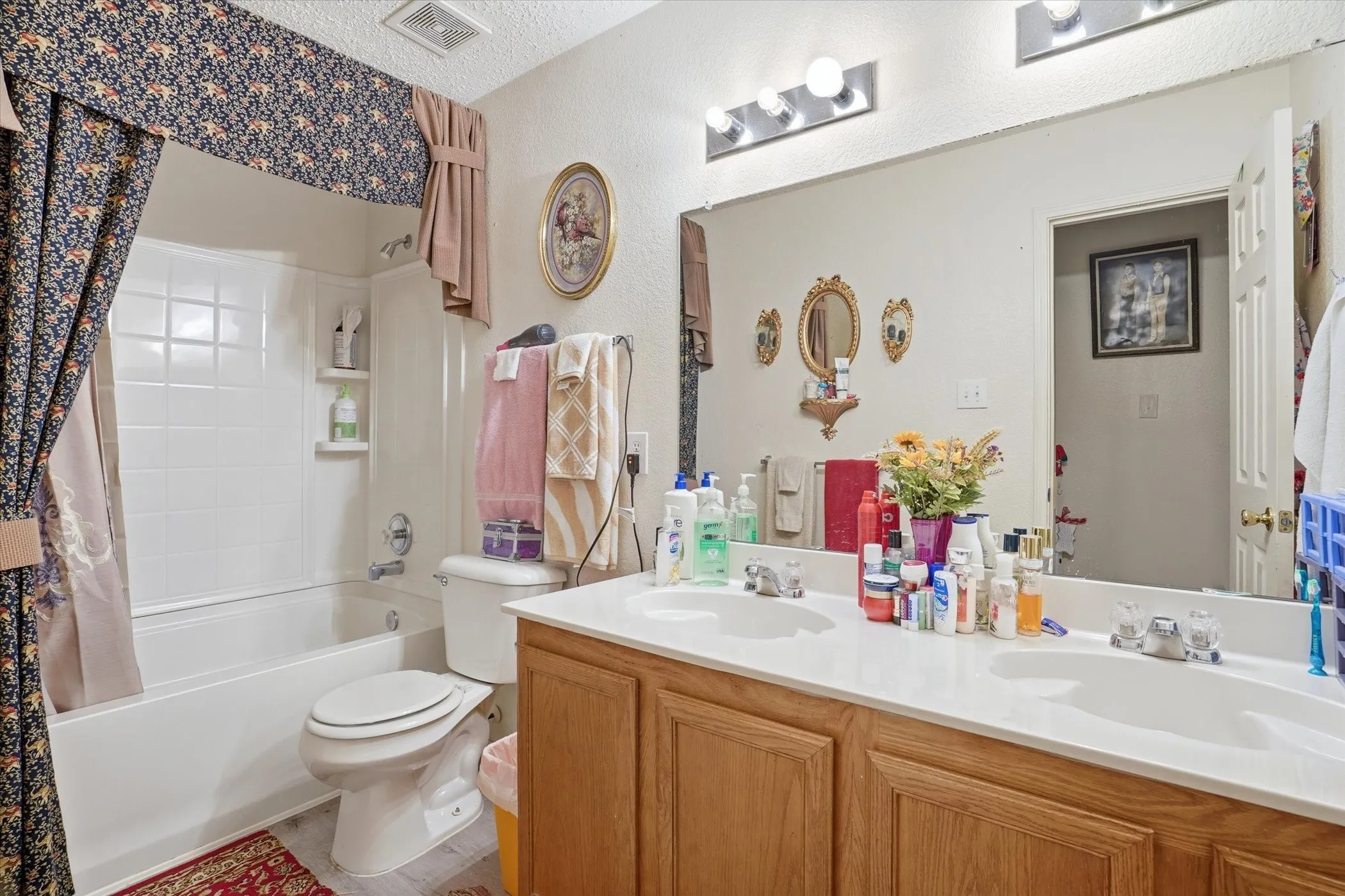 Full bathroom with double vanity, shower / bath combo with shower curtain, and a textured ceiling