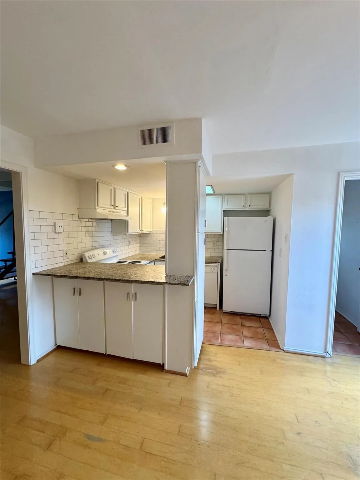 Kitchen featuring white appliances, light wood finished floors, white cabinetry, a peninsula, and decorative backsplash