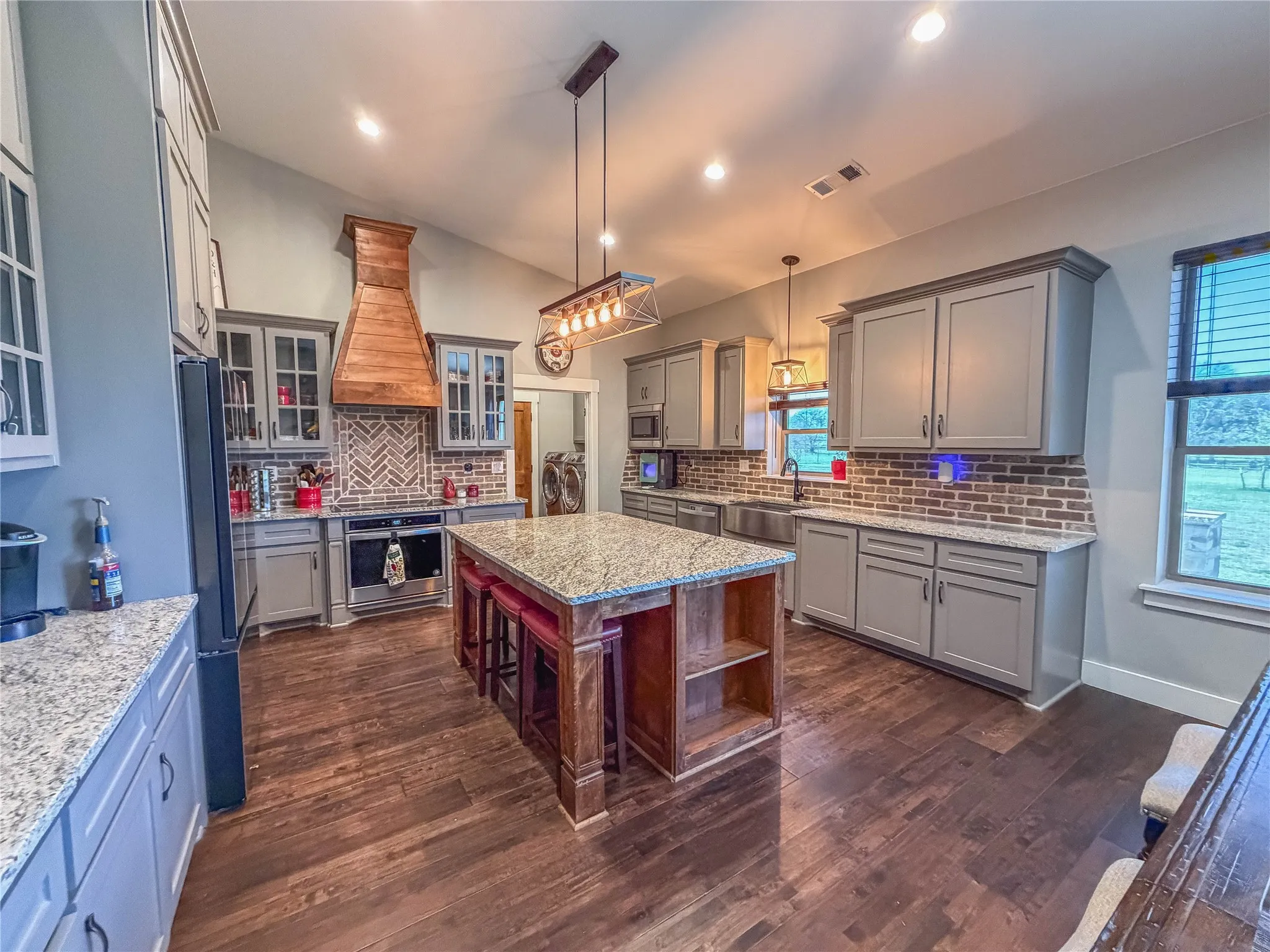Kitchen with glass fronted cabinets, light stone countertops, decorative light fixtures, backsplash, and stainless steel appliances