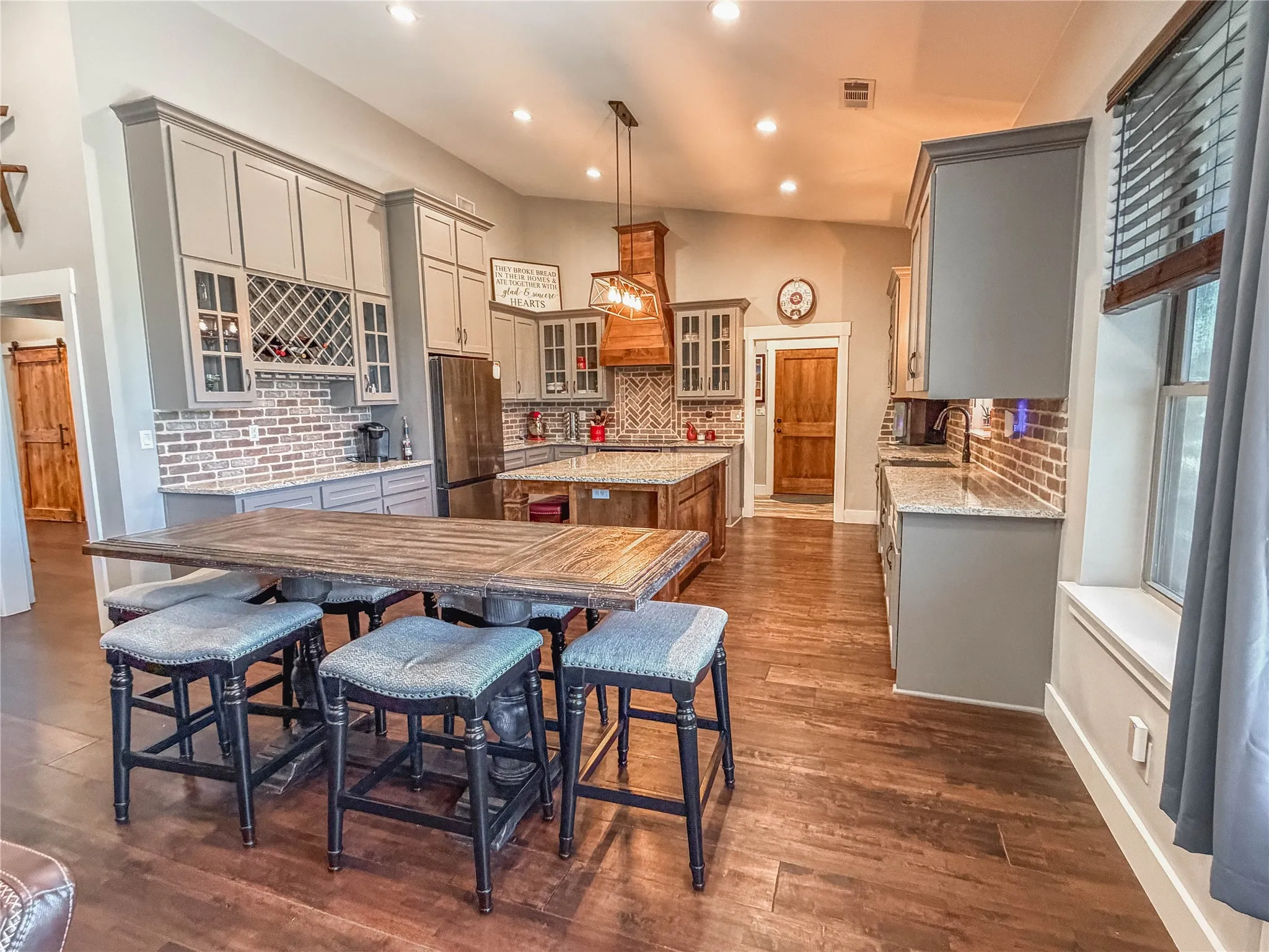 Dual tone kitchen featuring glass fronted cabinets, light stone countertops, a kitchen island, freestanding refrigerator, and dark wood-style flooring