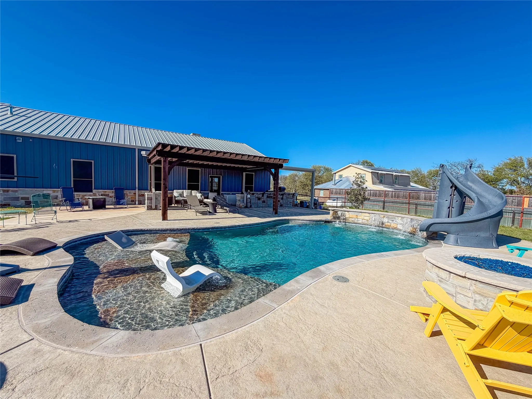 View of pool with an outdoor fire pit, a water slide, patio surround, and a fenced backyard