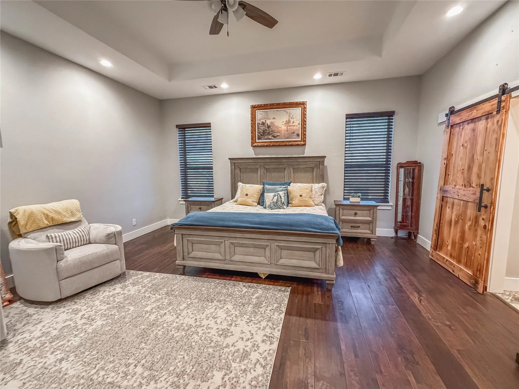 Bedroom featuring a barn door, dark wood-type flooring, a tray ceiling, ceiling fan, and recessed lighting
