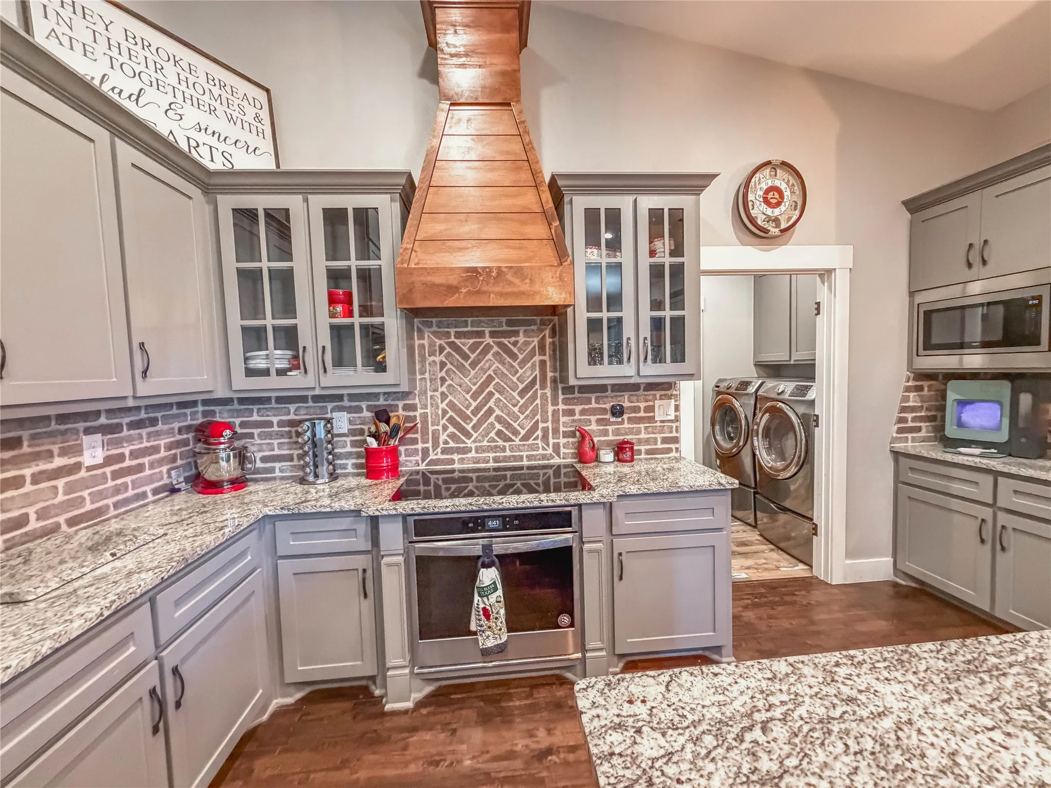 Kitchen with gray cabinetry, washer and clothes dryer, stainless steel appliances, dark wood-style flooring, and vaulted ceiling